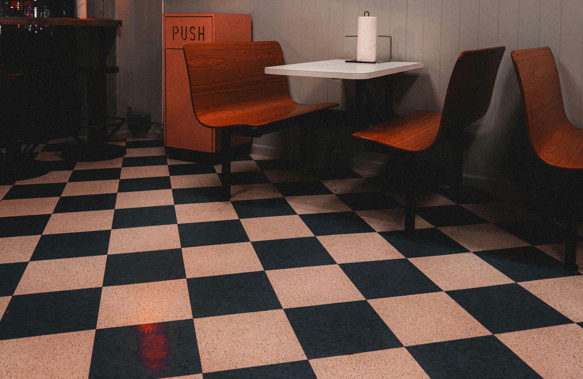 Classic black-and-white checkered tiles lend a retro diner vibe, perfectly complementing warm wood seating and vintage decor.