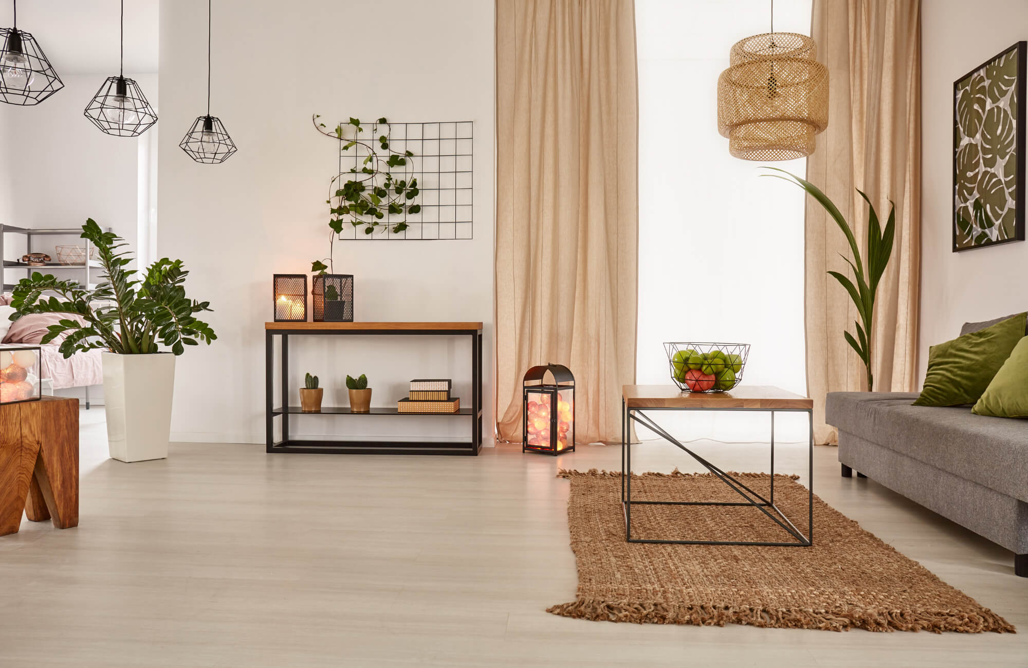 Modern living room with pendant lights, wicker chandelier, neutral curtains, indoor plants, and a jute rug for natural texture.