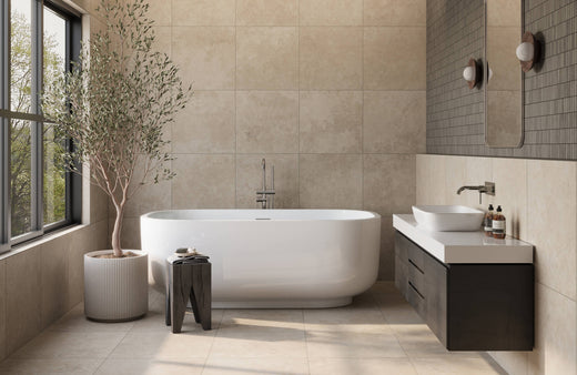 Modern bathroom with a freestanding white tub, floating vanity, large beige tiles, and a potted tree near floor-to-ceiling windows.