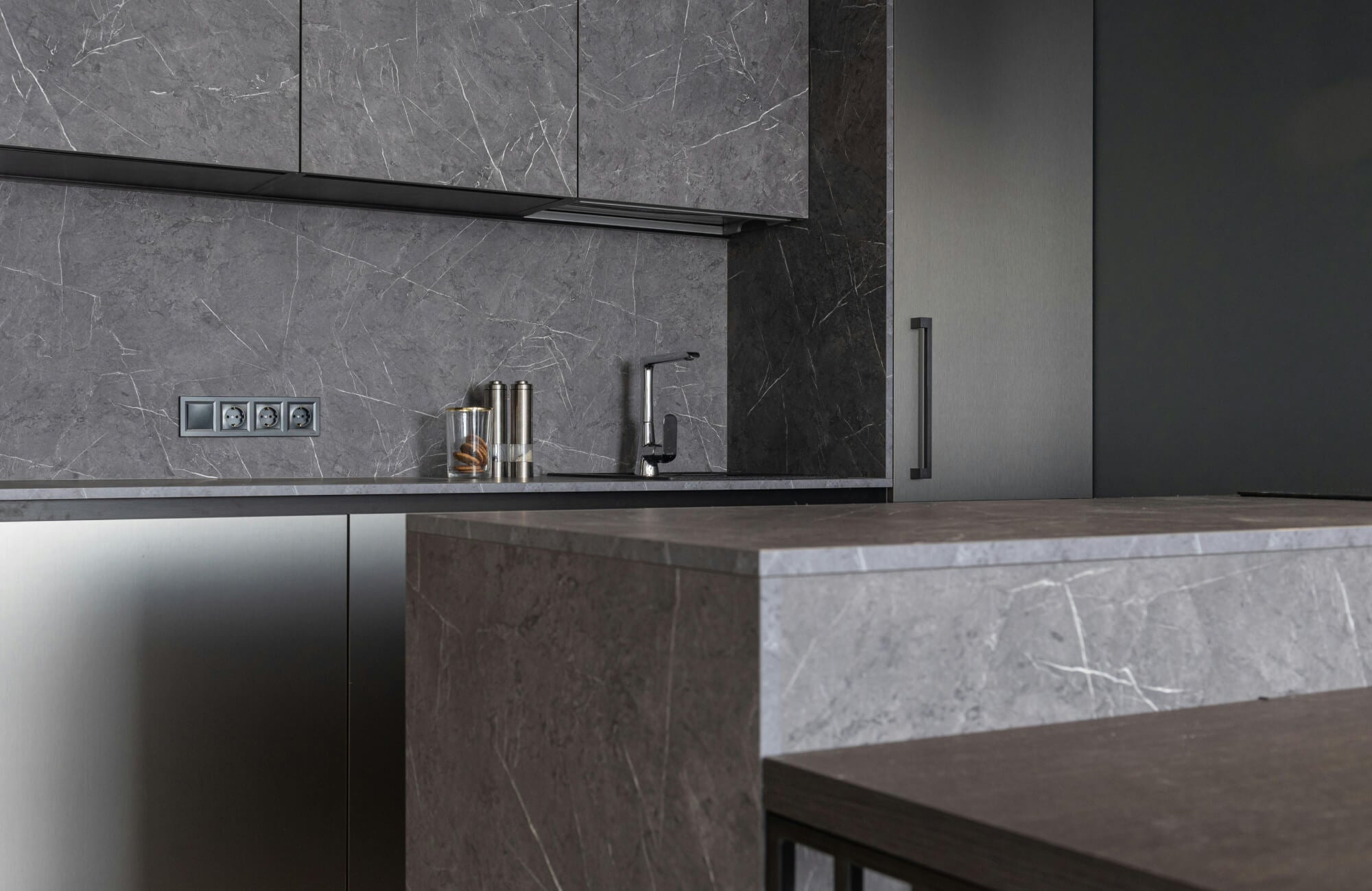 Sleek modern kitchen featuring grey marble countertops with striking white veining, complemented by stainless steel cabinetry and dark accents.