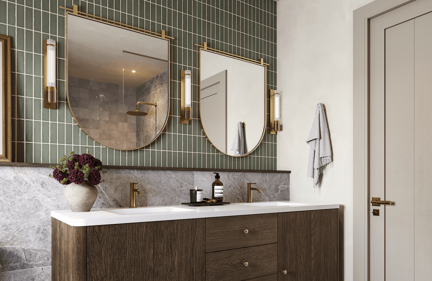 Double sink vanity with wood cabinetry, brass wall sconces, and vertical sage green tiles over a marble look backsplash.