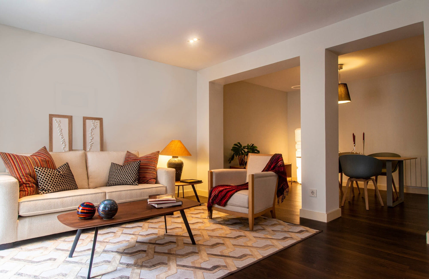 Modern living room with layered lighting, featuring recessed ceiling lights, a table lamp, and a pendant over the dining area.