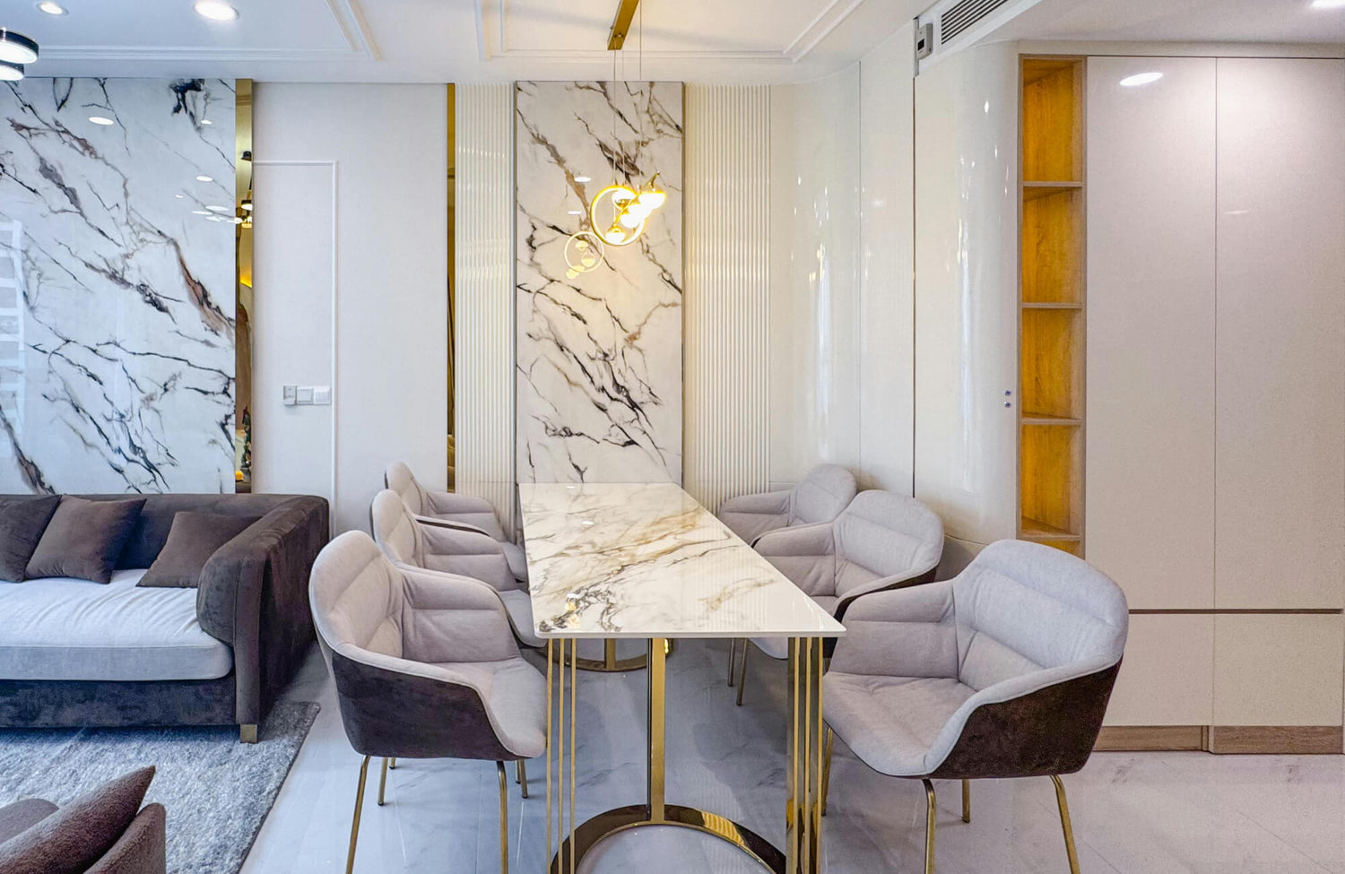Elegant modern dining area featuring a rectangular marble dining table with a polished white surface and bold gray veining, paired with upholstered chairs and gold metal legs.