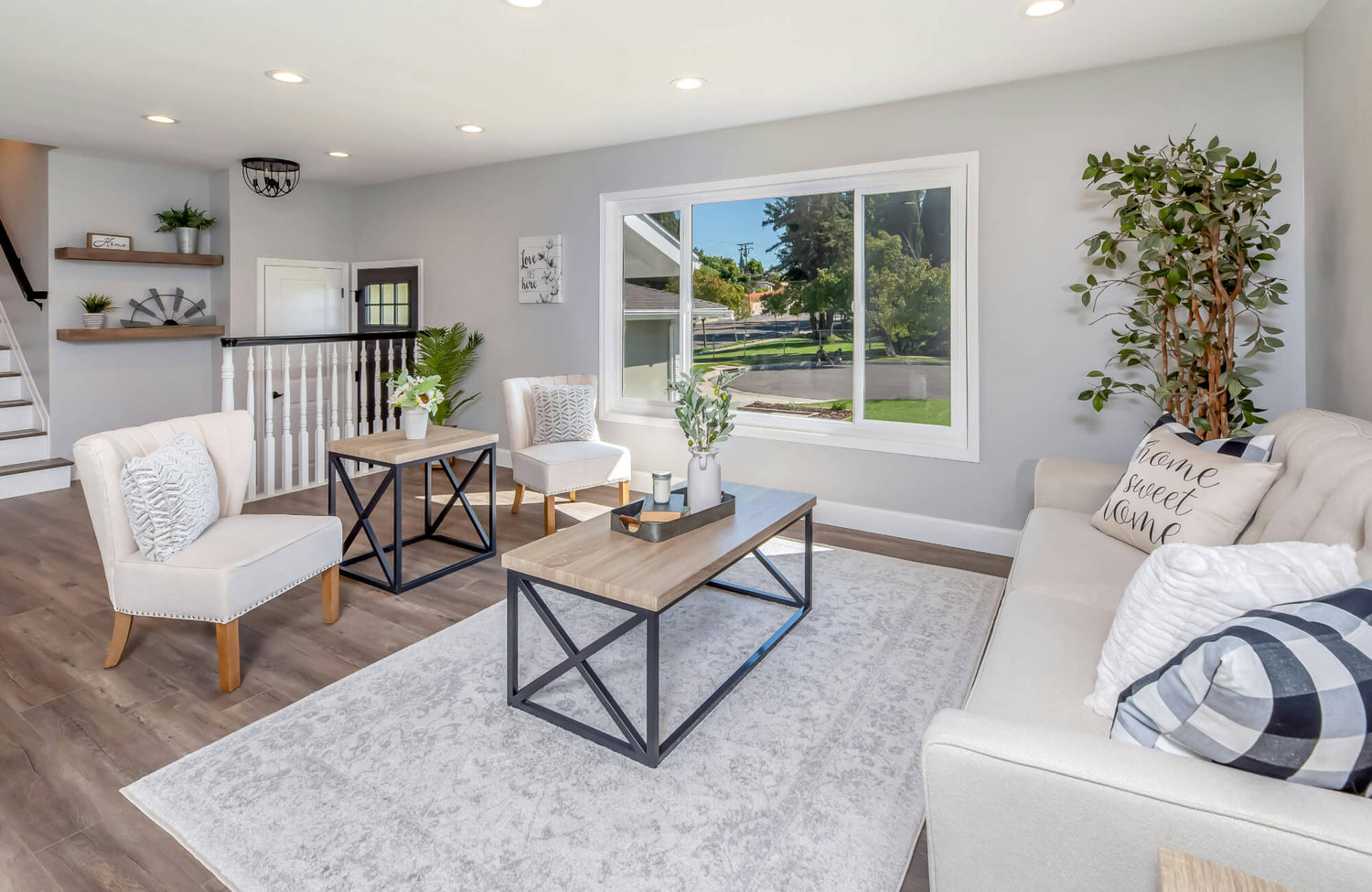 Bright modern living room with wood-look flooring and a soft grey patterned rug, paired with neutral furniture and a large window.