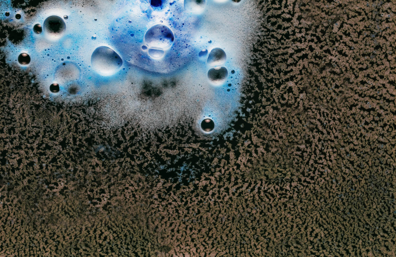 Washable rug being cleaned, with blue soap bubbles and foam creating a striking contrast against its textured brown surface.