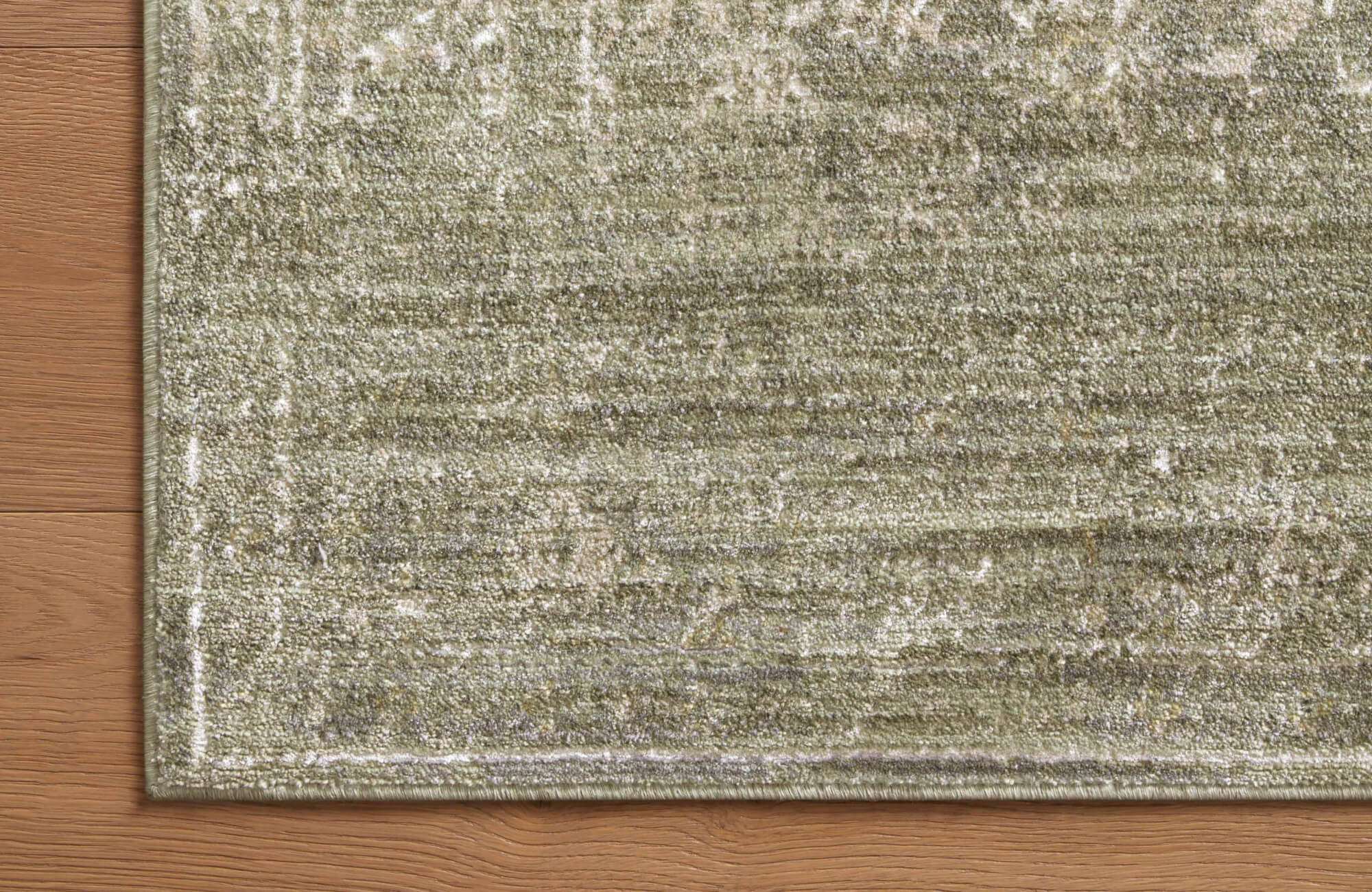 Detailed view of a green rug corner highlighting subtle tonal variation and plush texture as it meets natural wood floor planks.
