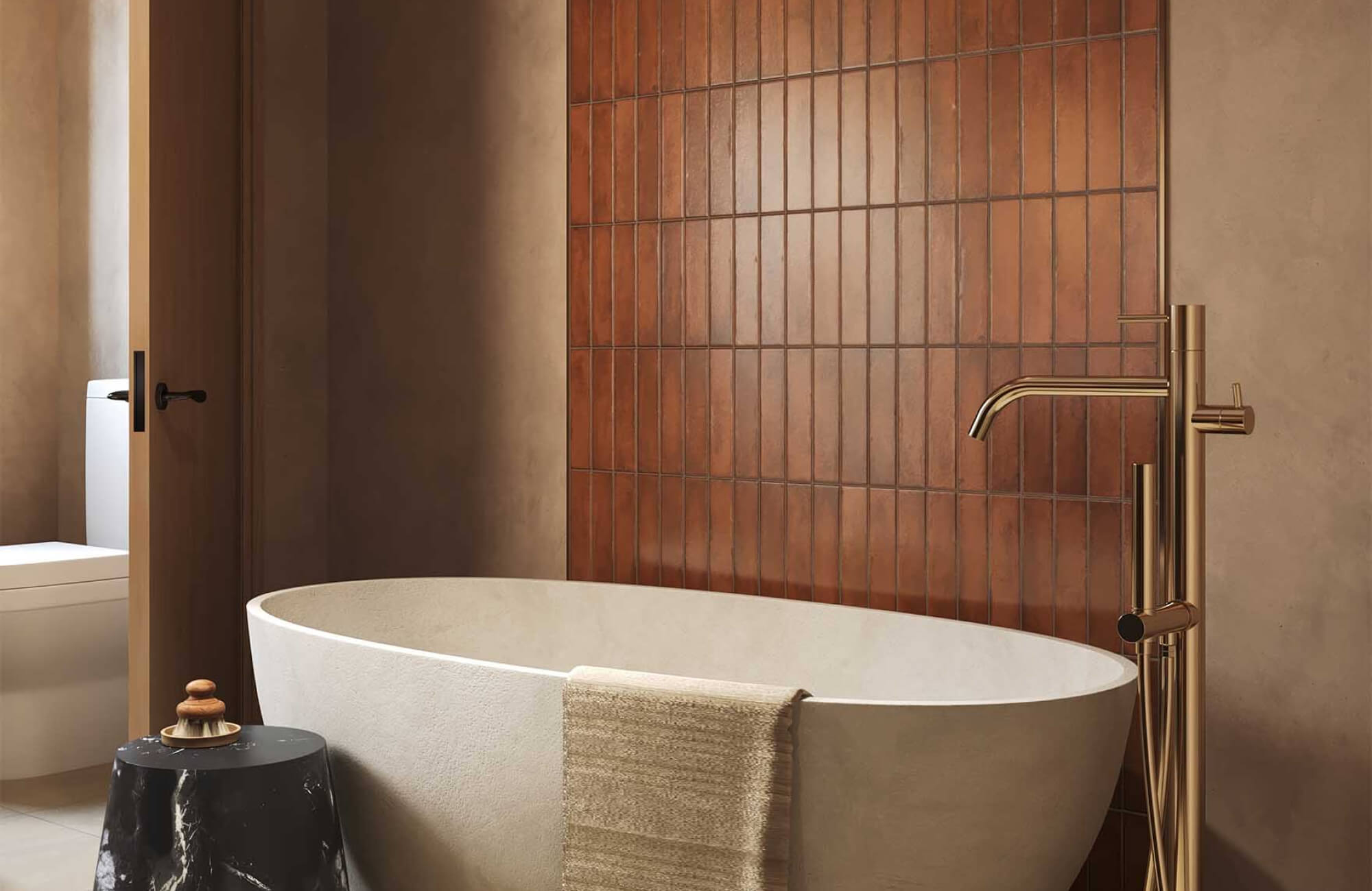 Modern bathroom with brown vertical subway tile accent wall, freestanding tub, brass fixtures, and warm, earthy tones.