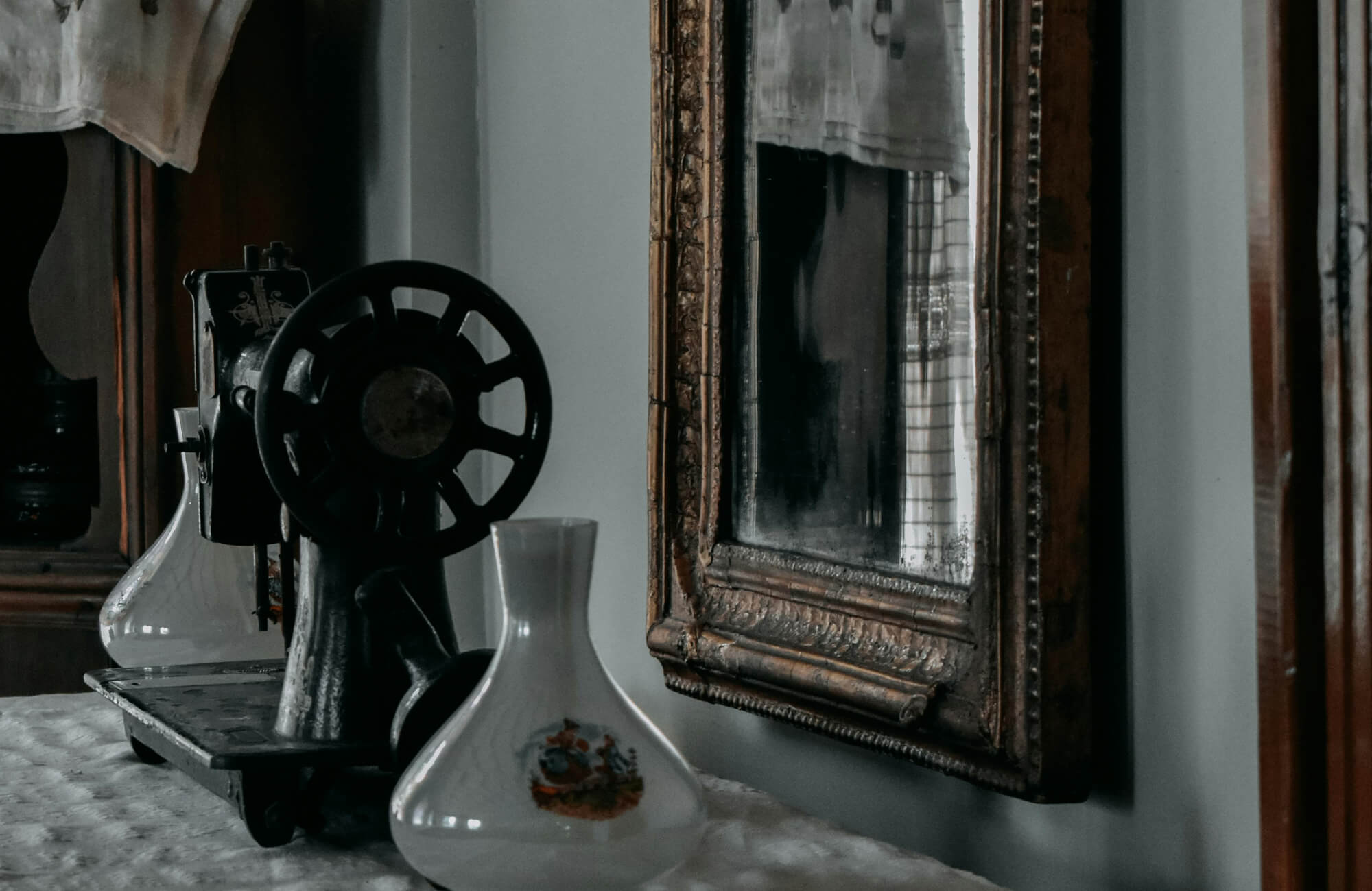 Close-up of an aged vintage mirror with an ornate carved frame beside antique decor and a sewing machine.