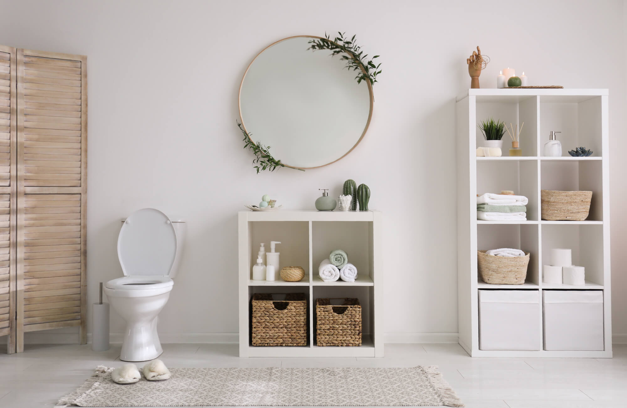 Modern bathroom with a round wall mirror, open shelving, wicker baskets, and minimalist decor in a soft, neutral color palette.