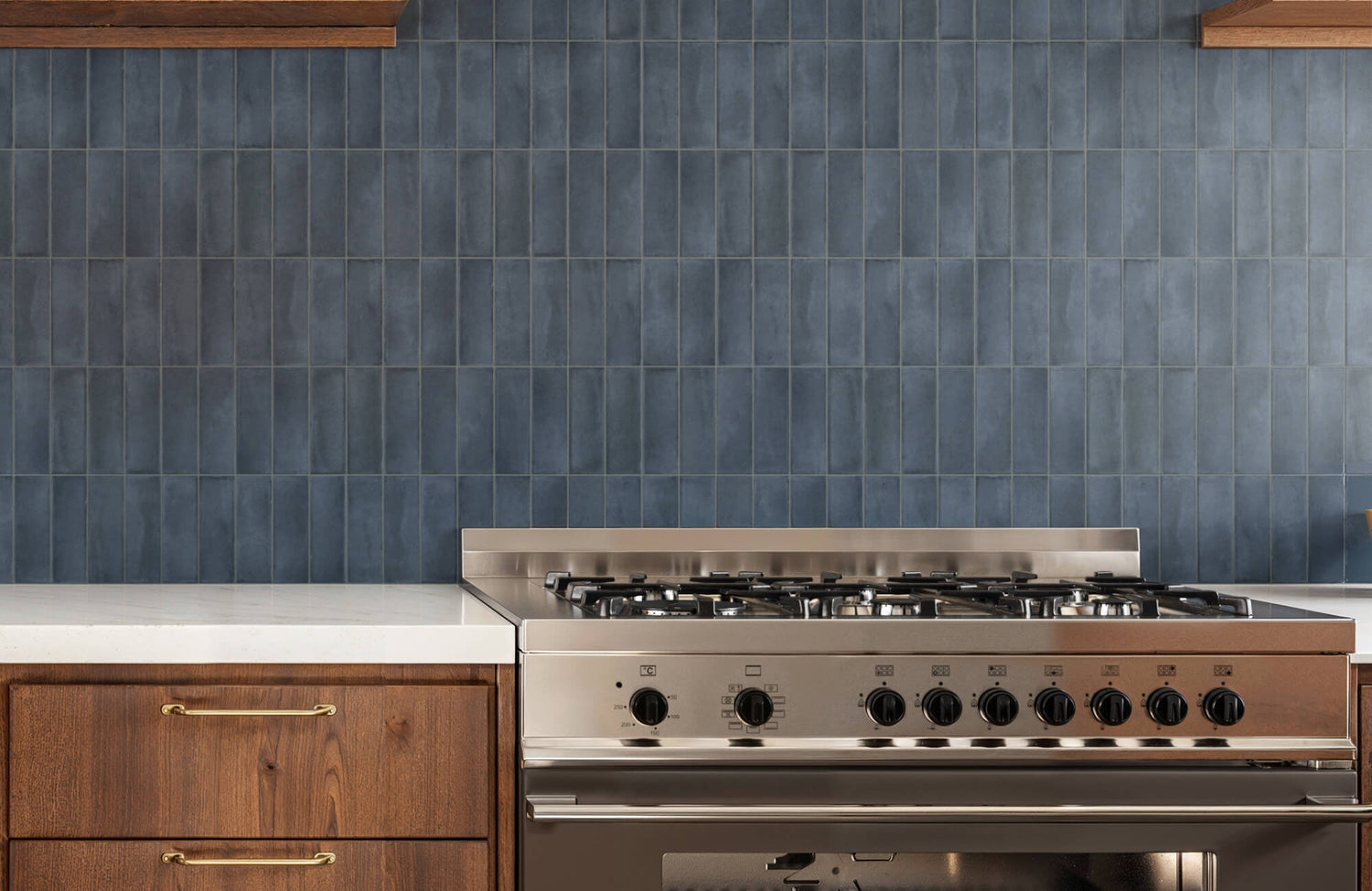 Rich navy porcelain backsplash tiles add depth and sophistication to a modern kitchen with walnut cabinetry and stainless-steel range.