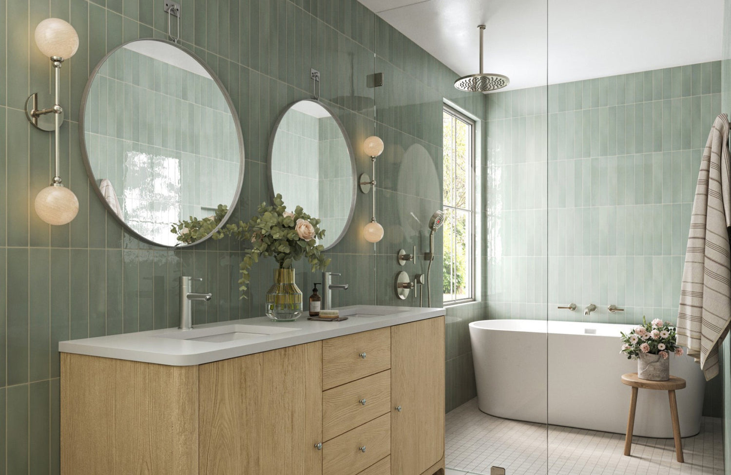 Twin globe wall sconces mounted beside round mirrors in a sage green tile bathroom with a double vanity.