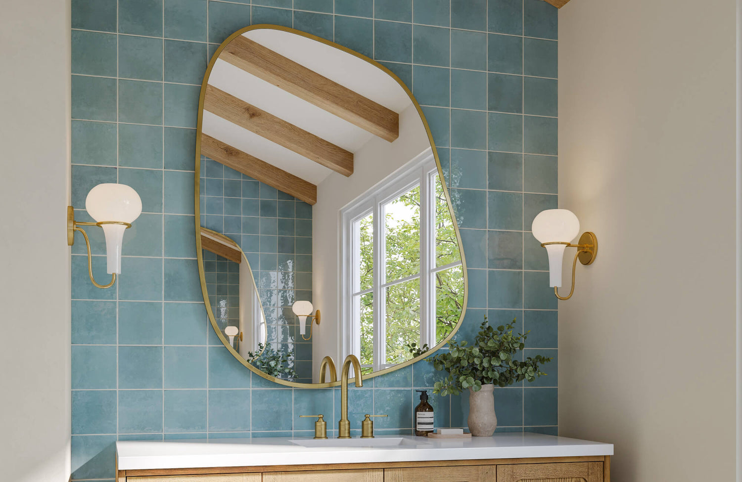 Curved statement mirror framed in gold reflects a bright window and ceiling beams, set against soft blue tile in a warm-toned bathroom.