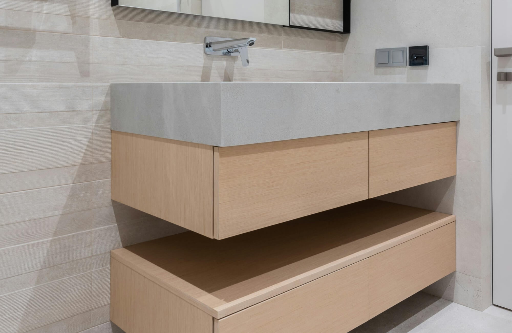Wall mounted bathroom vanity with light wood drawers and a sleek gray stone countertop, creating a modern and minimalist aesthetic.