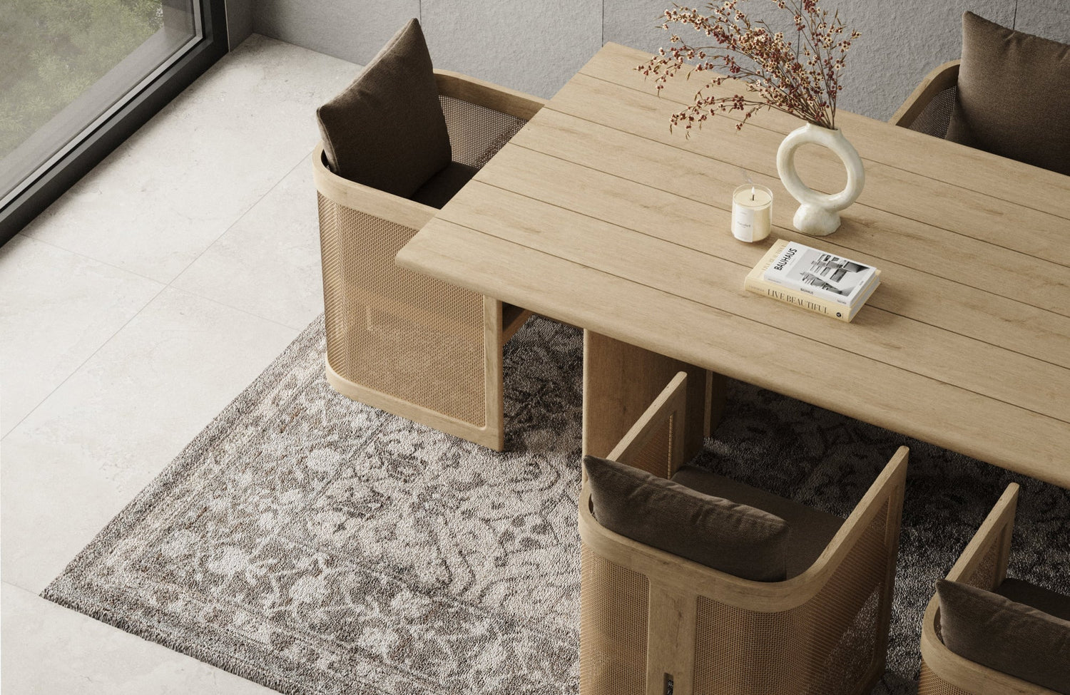 Dining area with light wood table and woven chairs set over a textured gray rug on pale stone flooring beside a window.