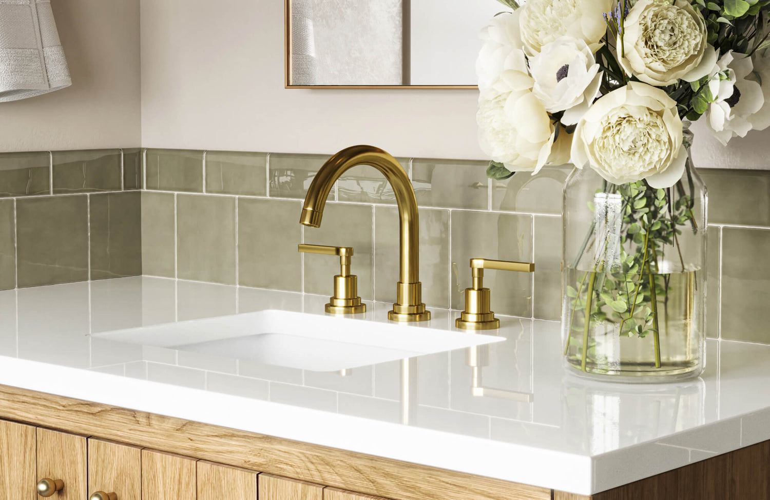 Glossy sage green square backsplash tiles frame a sleek white vanity top, accented by a gold faucet and fresh floral arrangement.