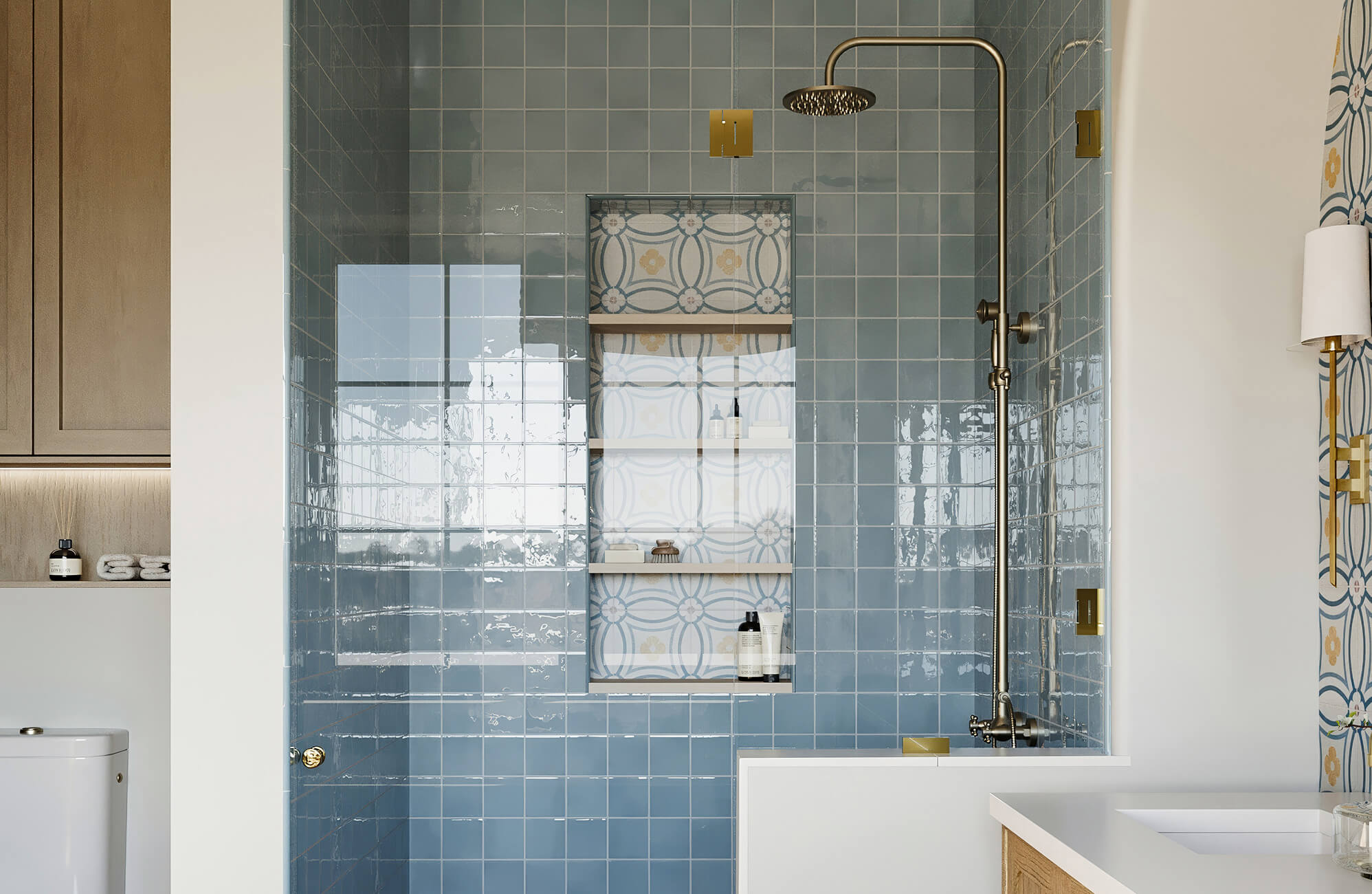 Glossy sky-blue ceramic shower tiles with a built-in shelf lined in retro floral tile, accented by brass fixtures.