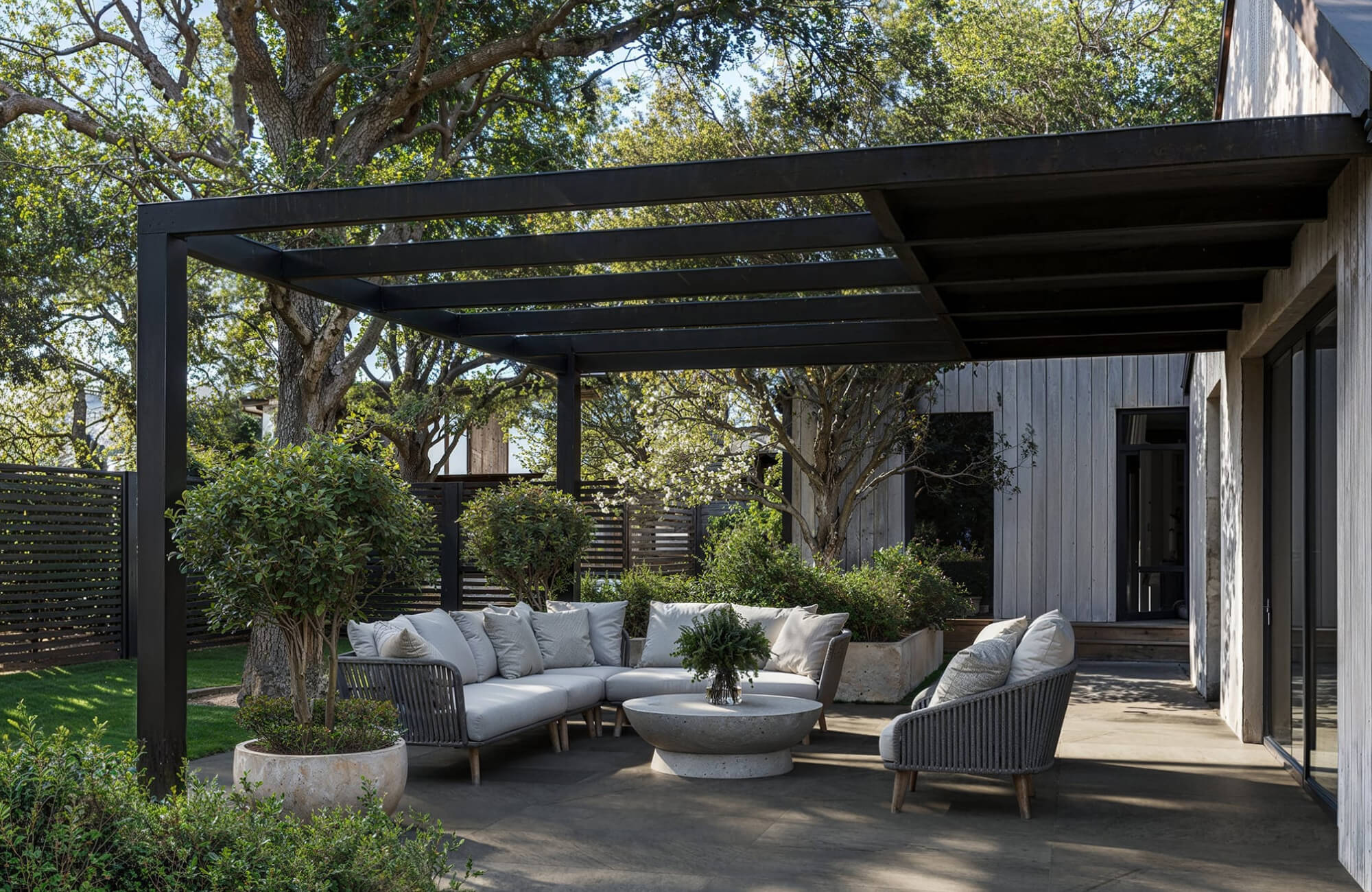 Warm-toned patio flooring beneath a modern pergola seating area surrounded by greenery.
