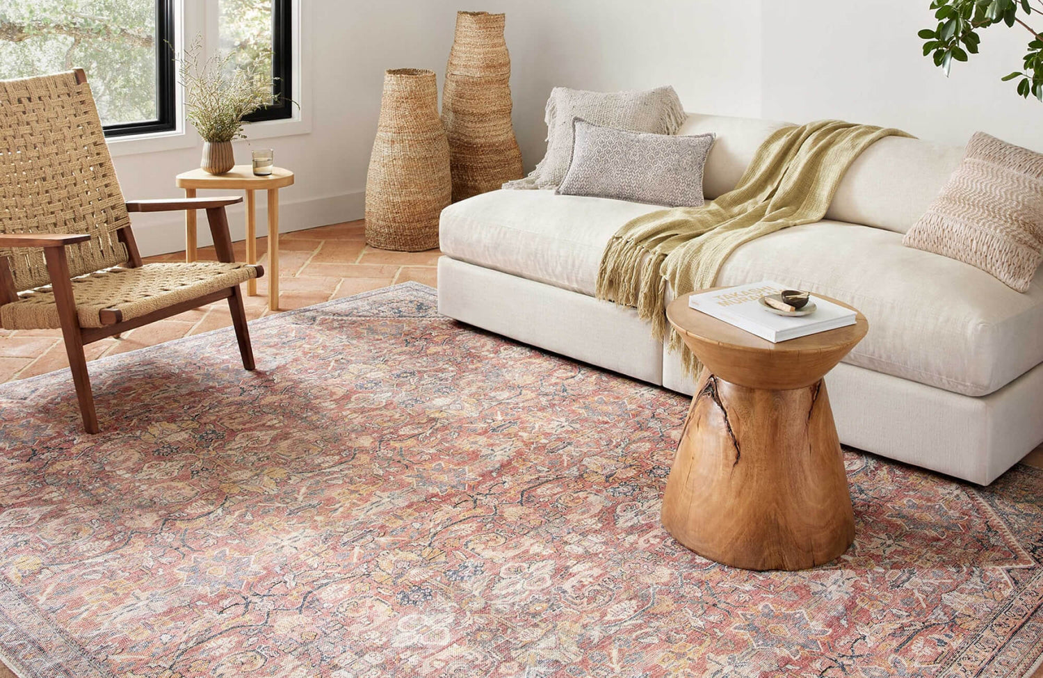 A cozy living space with terracotta floor tiles, a vintage rug, and natural wood and woven accents for a warm, rustic feel.