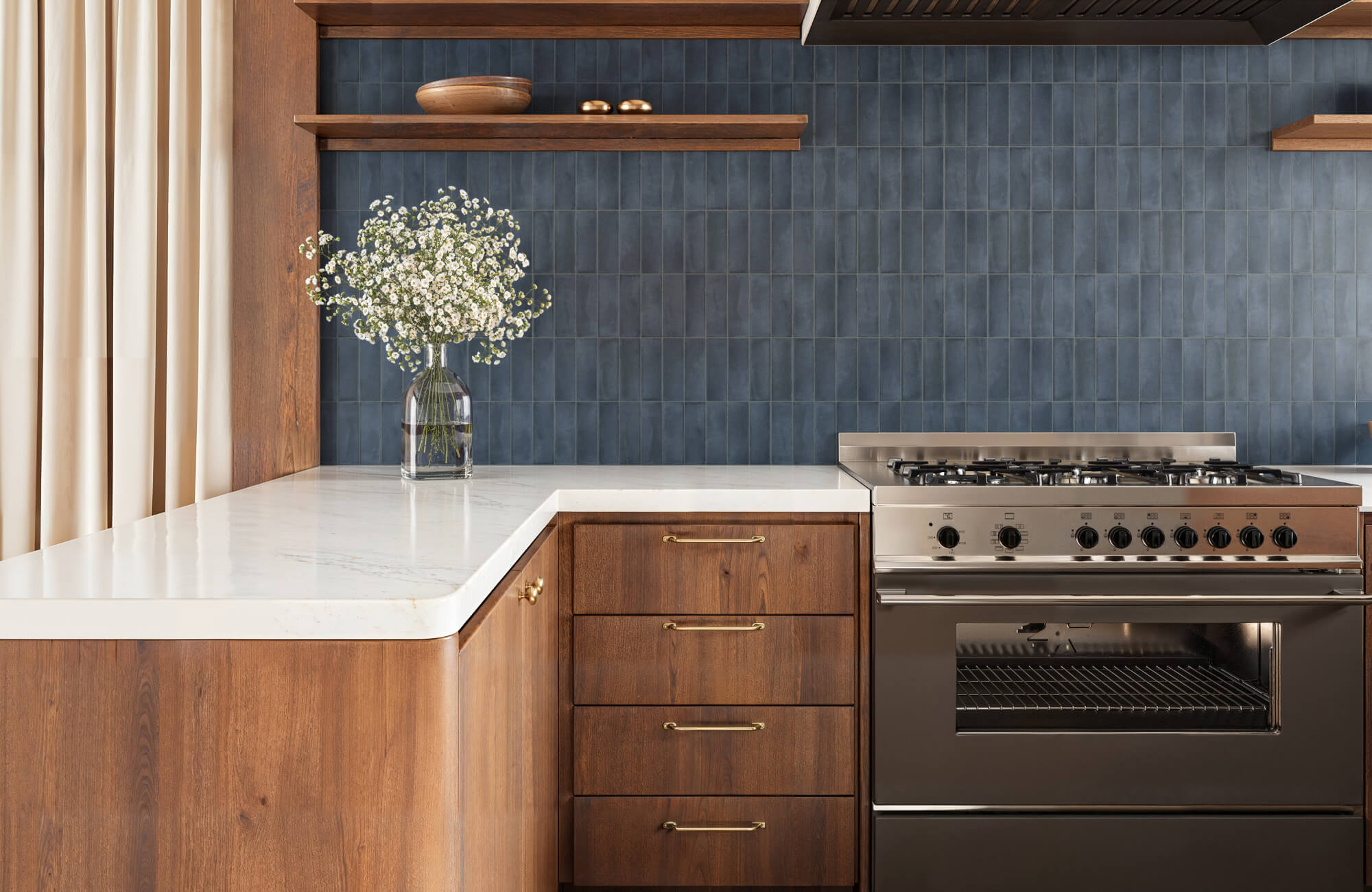 Stylish kitchen with rich wood cabinetry, navy blue subway tiled backsplash, marble countertops, and a stainless steel gas range.