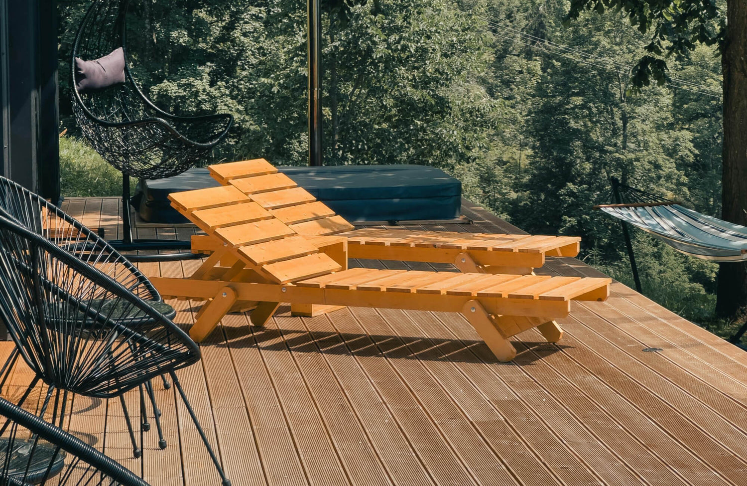 Relaxed outdoor deck with natural wood decking and outdoor flooring, furnished with wooden lounge chairs and woven seating, set against lush greenery for a serene, nature-inspired retreat.