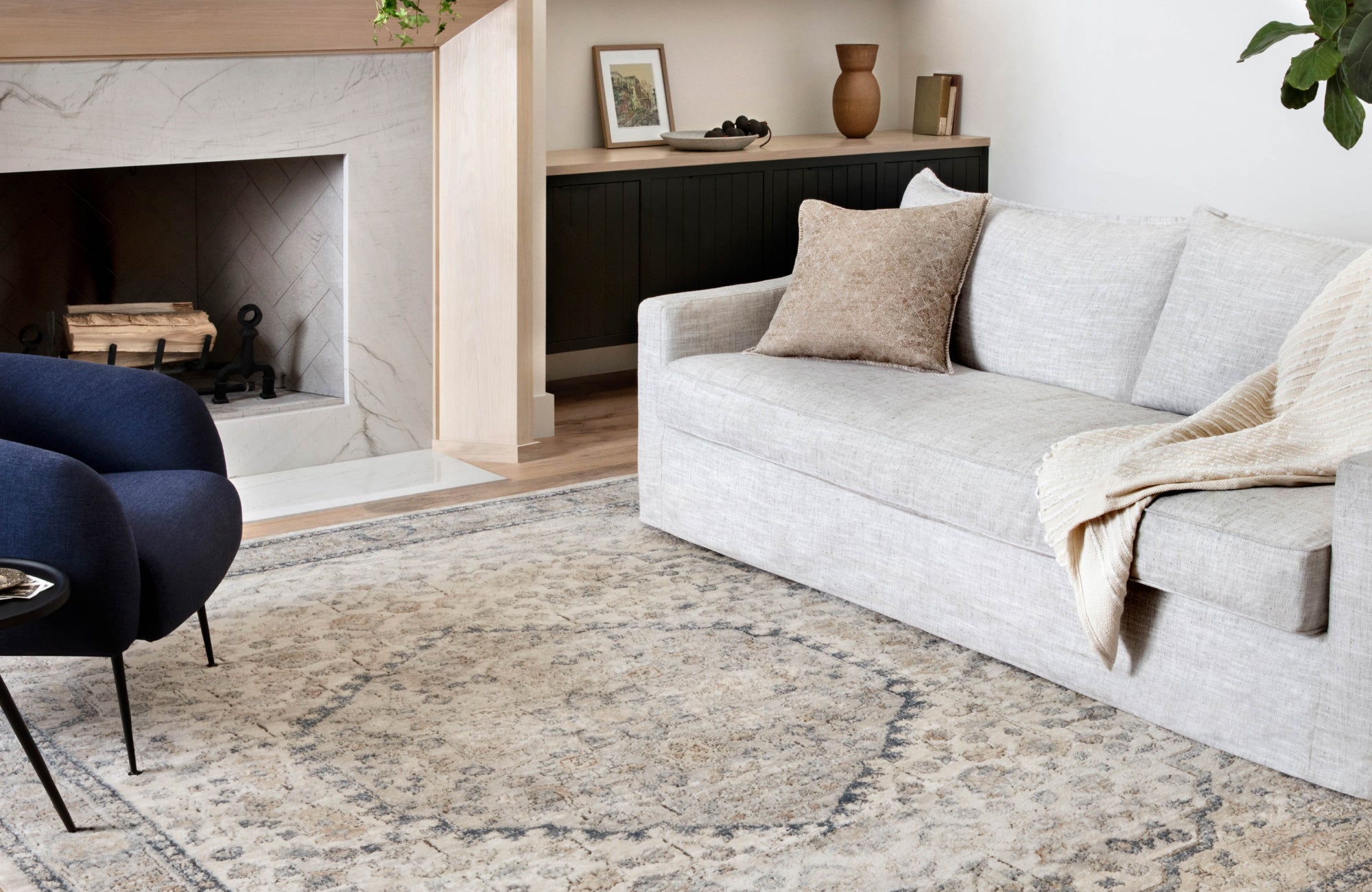 Neutral beige and gray rug in a soft-toned living room with a light stone fireplace and minimalist styling