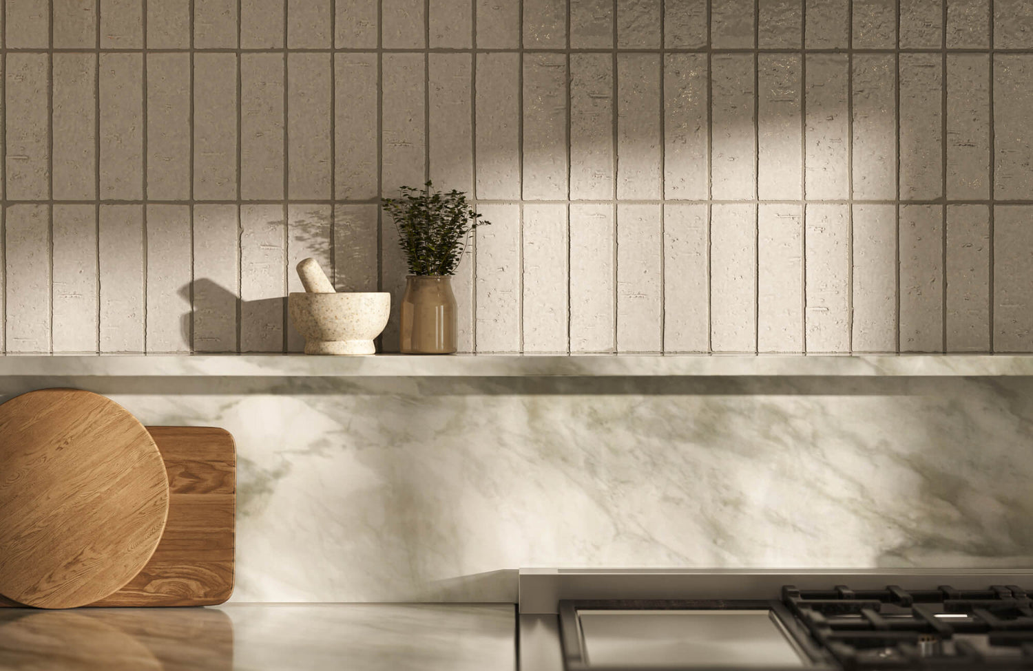 Neutral-toned kitchen wall with vertically stacked subway tiles and a marble shelf, accented by simple decor including a ceramic mortar and a small plant.