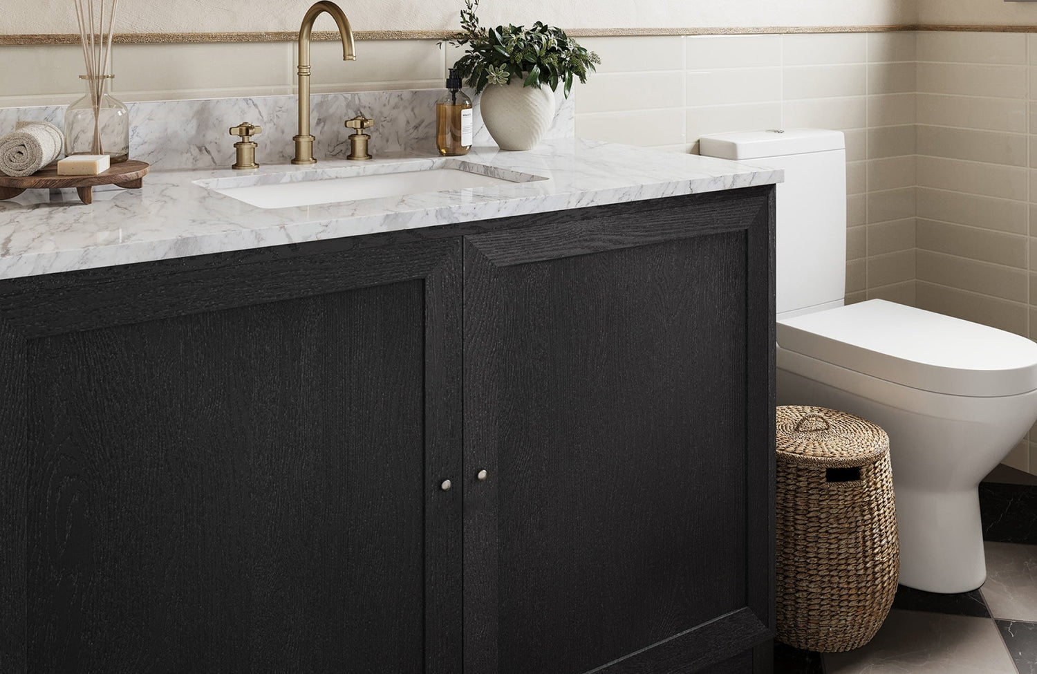 Dark wood bathroom vanity with marble top and gold faucet beside a modern toilet and woven basket on tiled floor