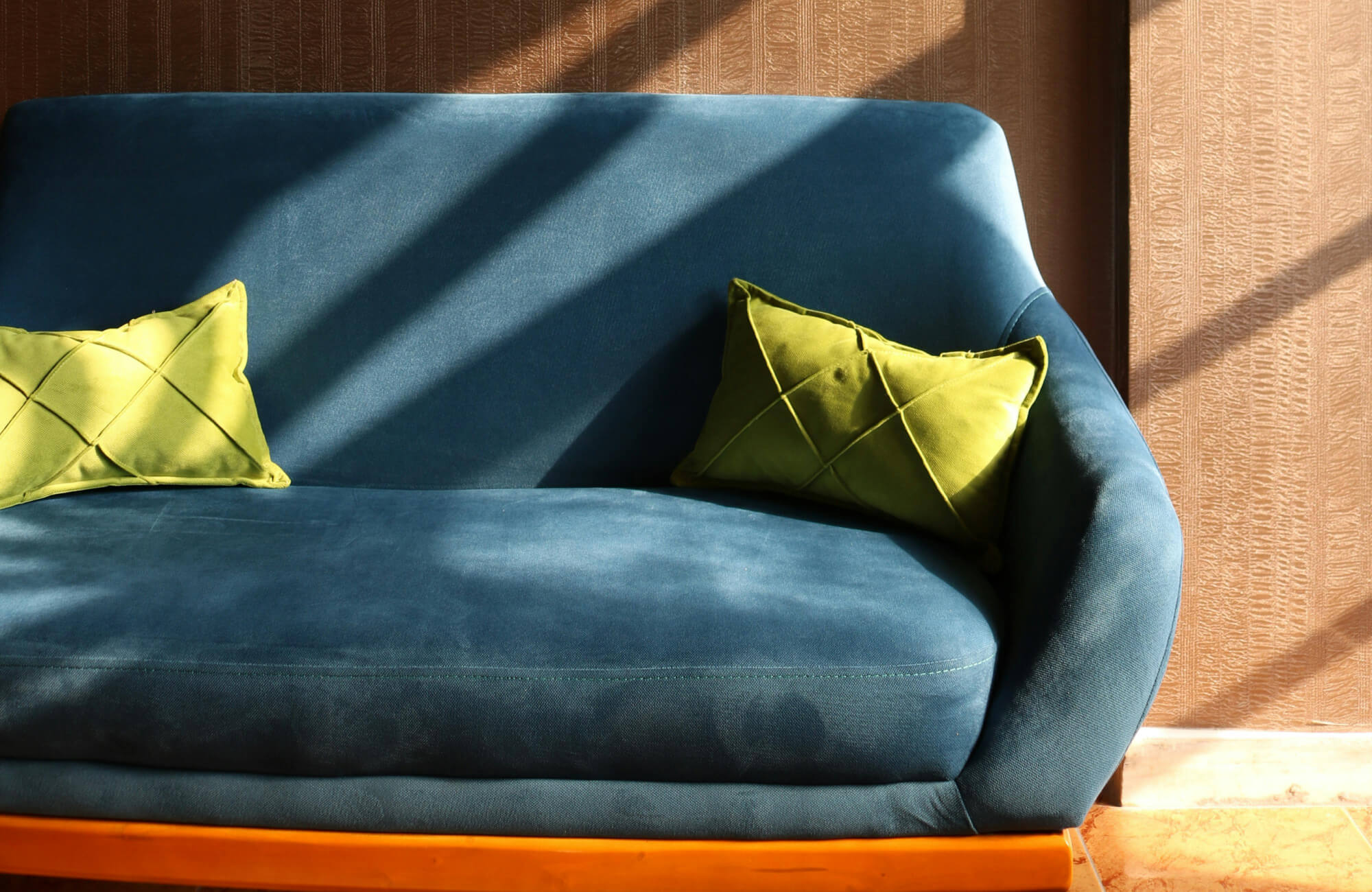 Bright green decorative pillows bring a lively contrast to the blue sofa, catching the light as shadows move across the surface.