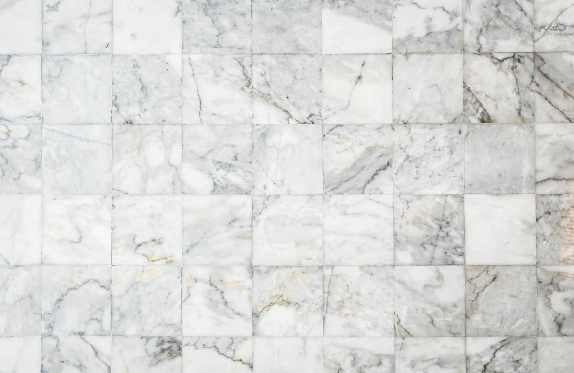 White marble tiles arranged in a grid pattern with soft gray veining and natural stone variation across the polished surface.