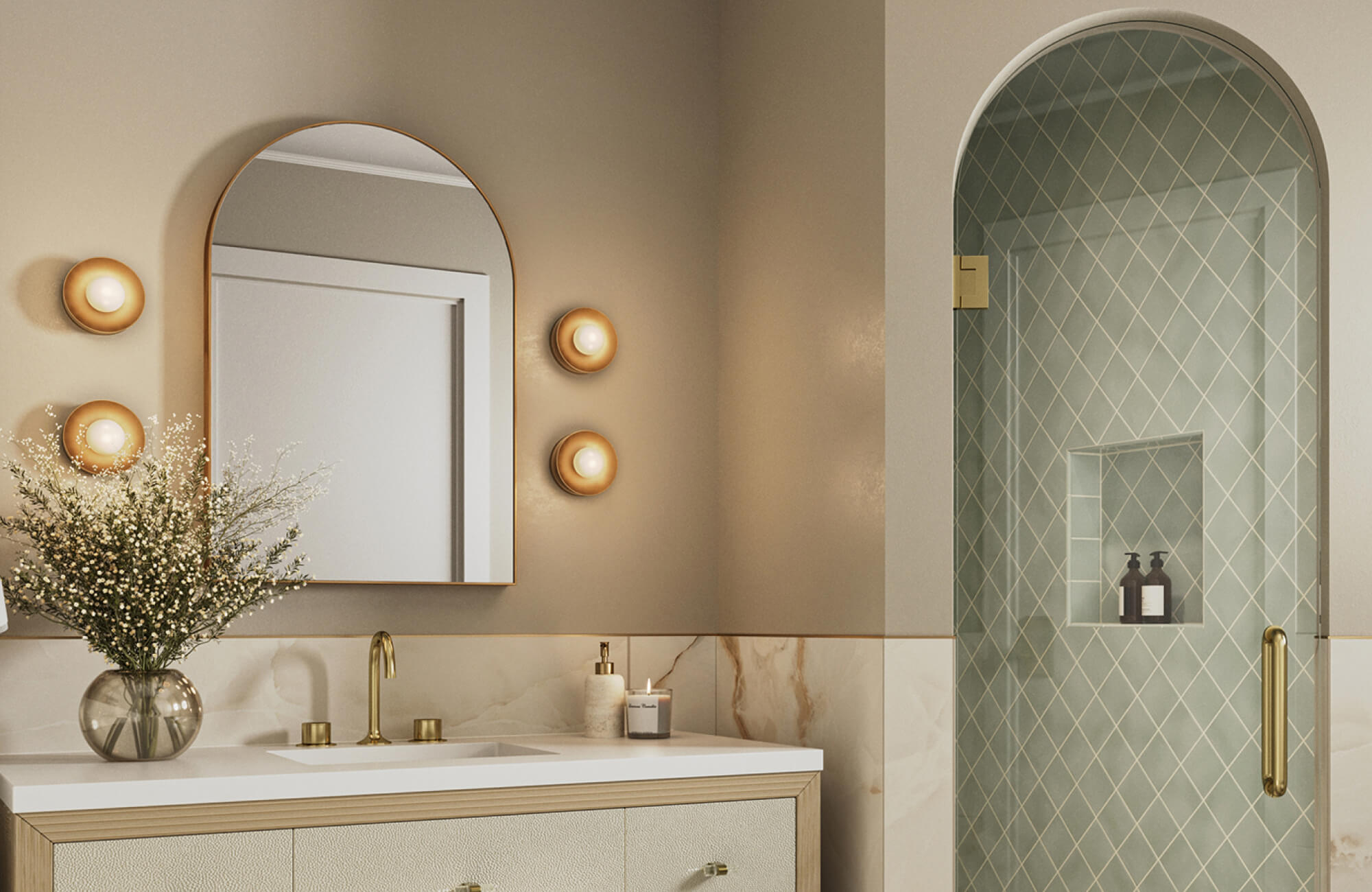 Elegant bathroom featuring an arched mirror with a gold frame, complemented by warm wall sconces, brass fixtures, and a glass shower with diamond-patterned green tiles.