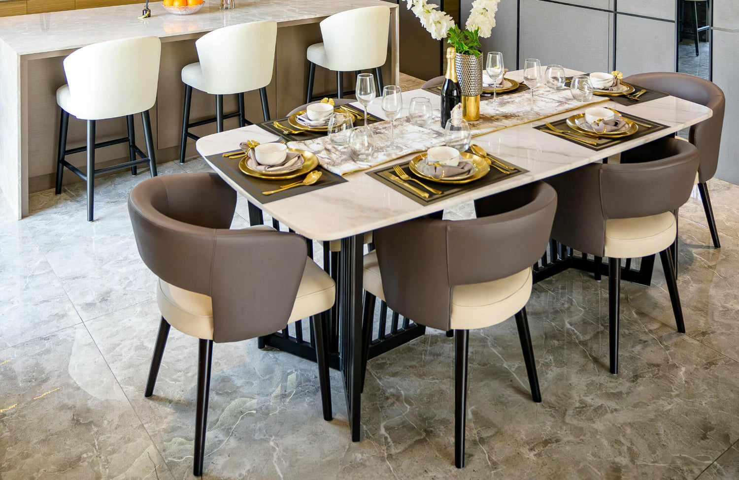 Elegant dining area with marble-look tile flooring, set table with gold accents, and modern upholstered chairs.