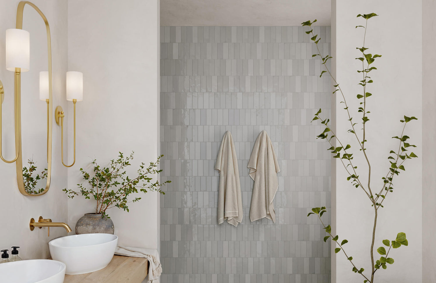 Vertical subway tile wall in a serene bathroom with brass fixtures and greenery for a calm, modern aesthetic.