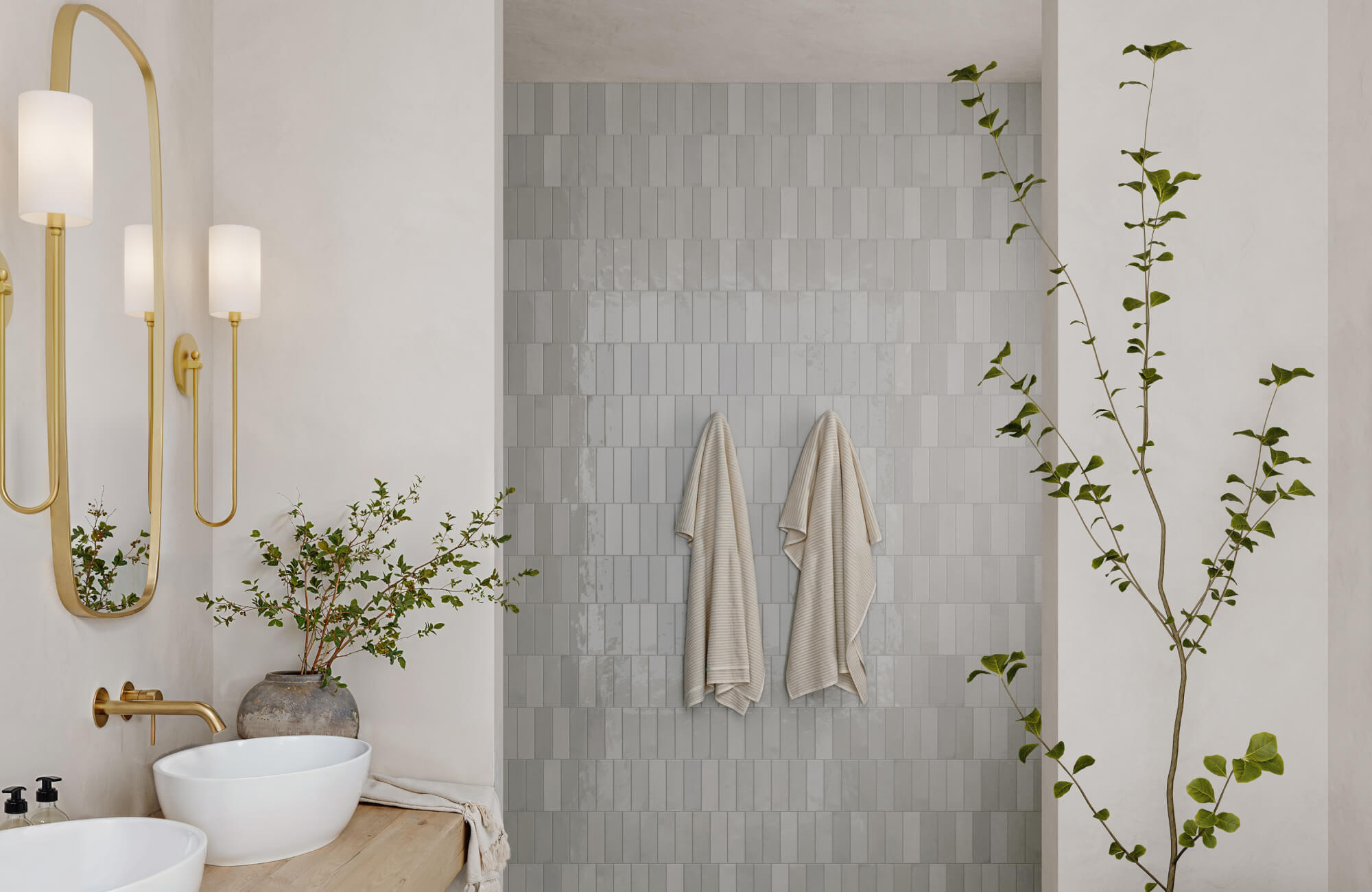 Vertical subway tile wall in a serene bathroom with brass fixtures and greenery for a calm, modern aesthetic.