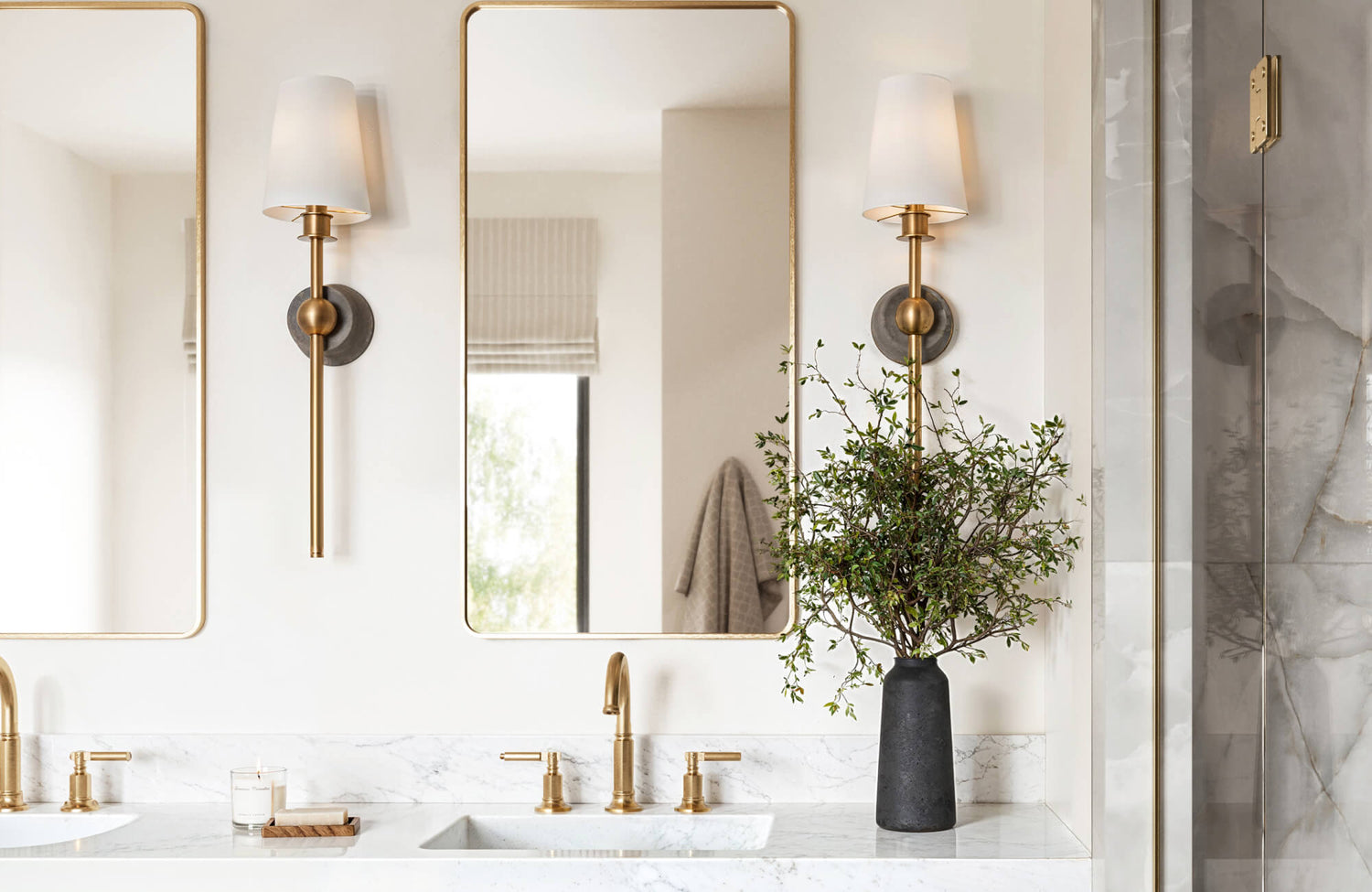 Brass wall sconces and mirrors accent a marble double vanity with ambient lighting and modern fixtures.