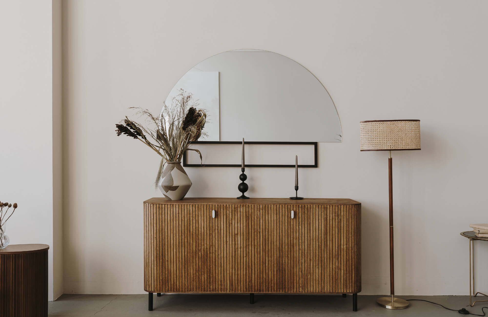 Wooden sideboard with a large half-round mirror, dried florals, and candles styled against a soft neutral wall.