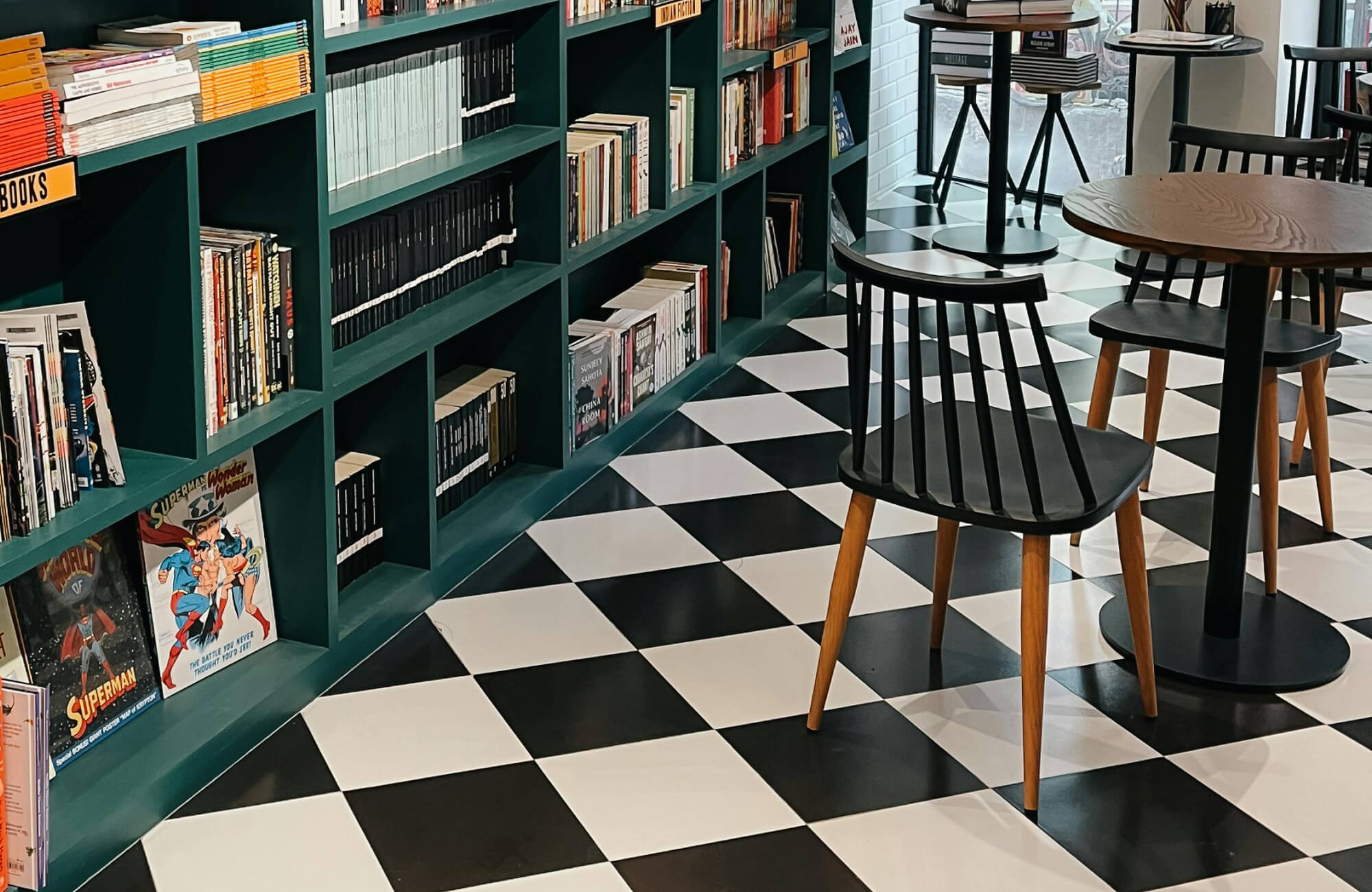 Stylish bookstore café with bold black and white checkered floor tiles, deep green bookshelves, and sleek black chairs for a cozy reading vibe.