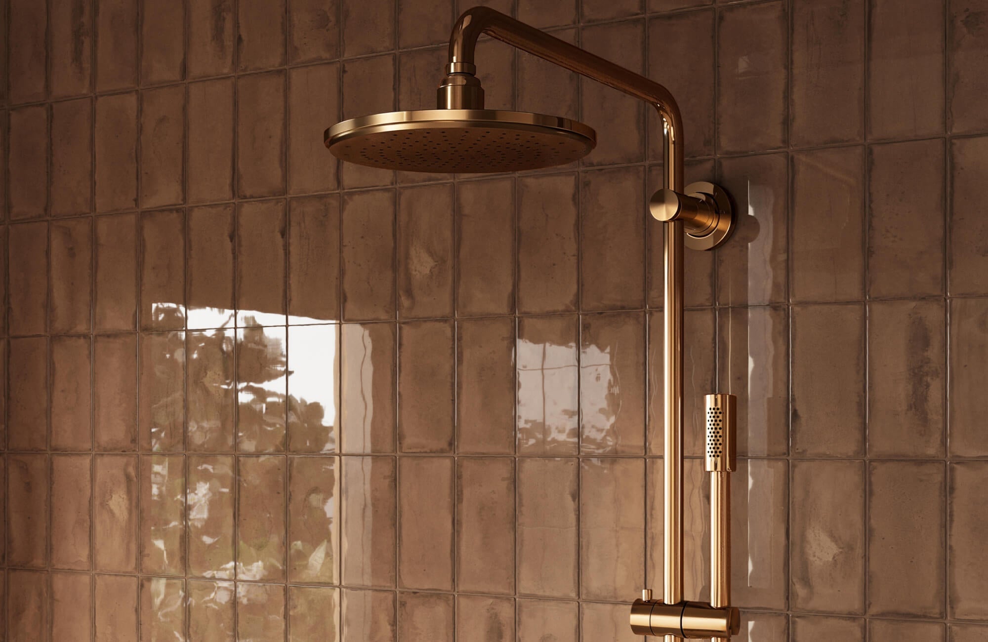 Close-up of a brass rainfall shower head mounted on a glossy brown subway tile shower wall, with vertical rectangular tiles reflecting soft window light.