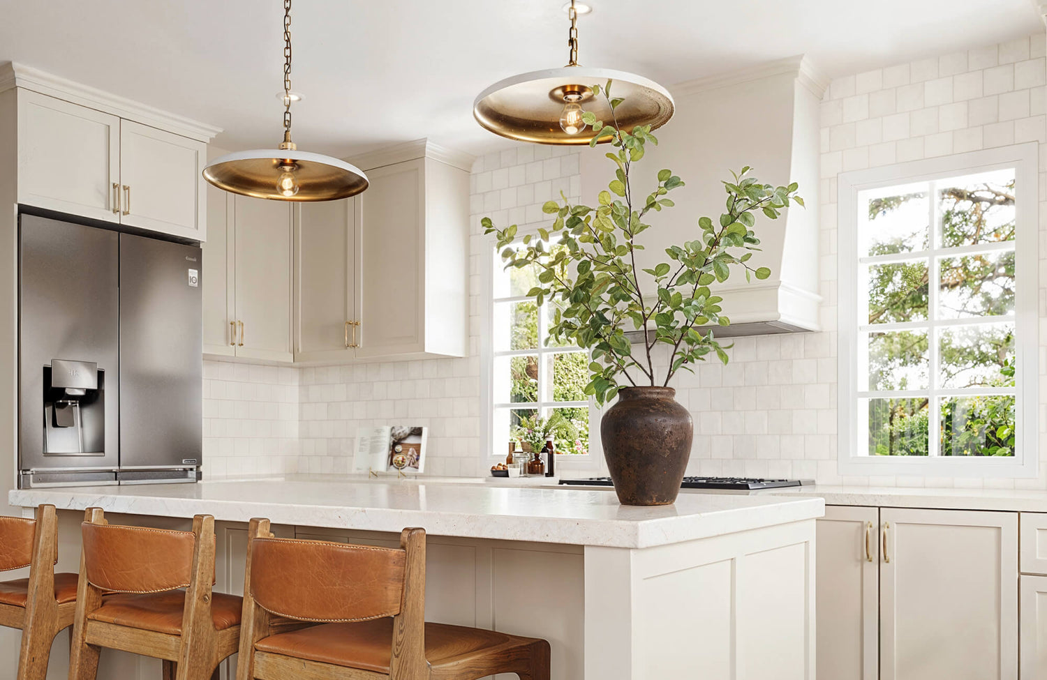 Kitchen with off-white cabinets, square tile backsplash, quartz counters, leather stools, and brass pendant lights