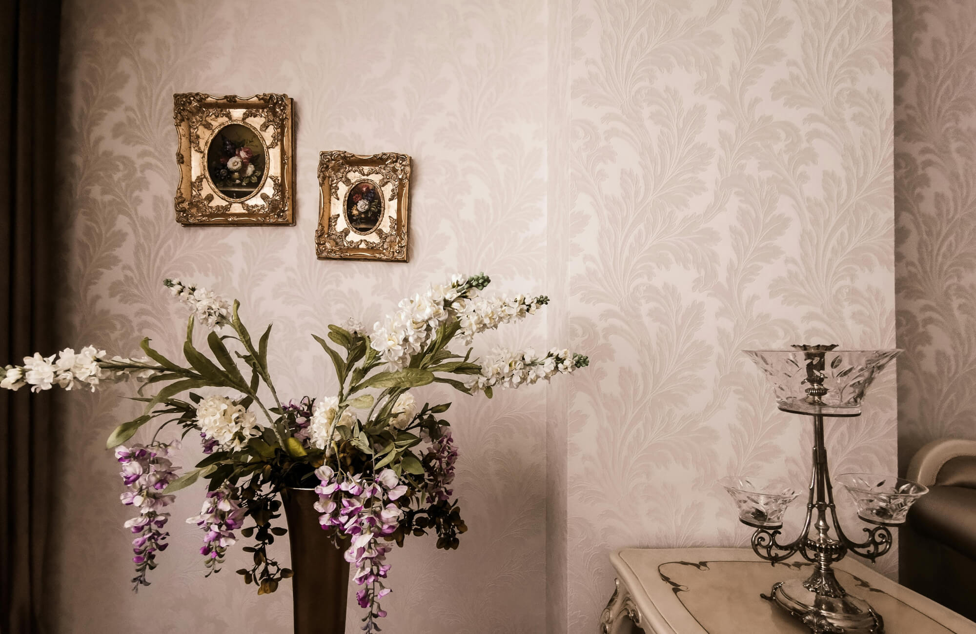 Elegant beige damask wallpaper with ornate frames and floral arrangement, styled on a classic console table for a refined traditional interior.