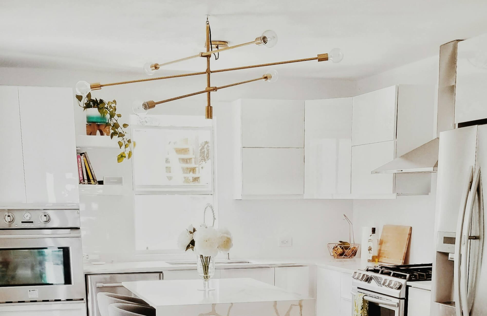 Bright white kitchen with glossy cabinets and modern gold statement lights adding elegance to the space.