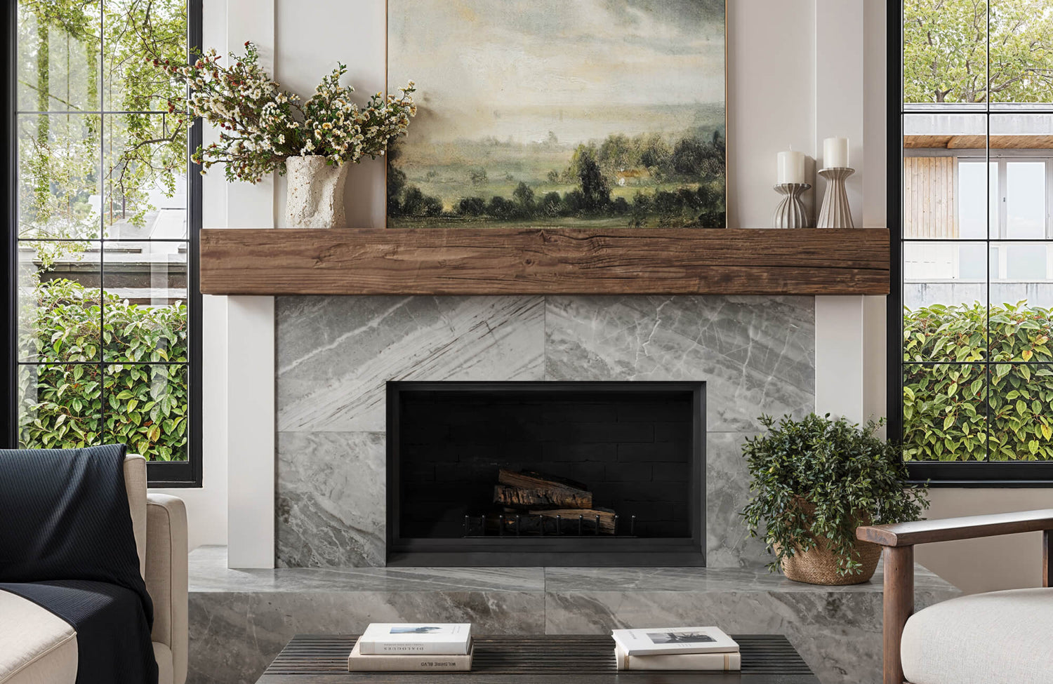 Modern fireplace clad in marble look tile with wood mantel and landscape art in a cozy, contemporary living room.