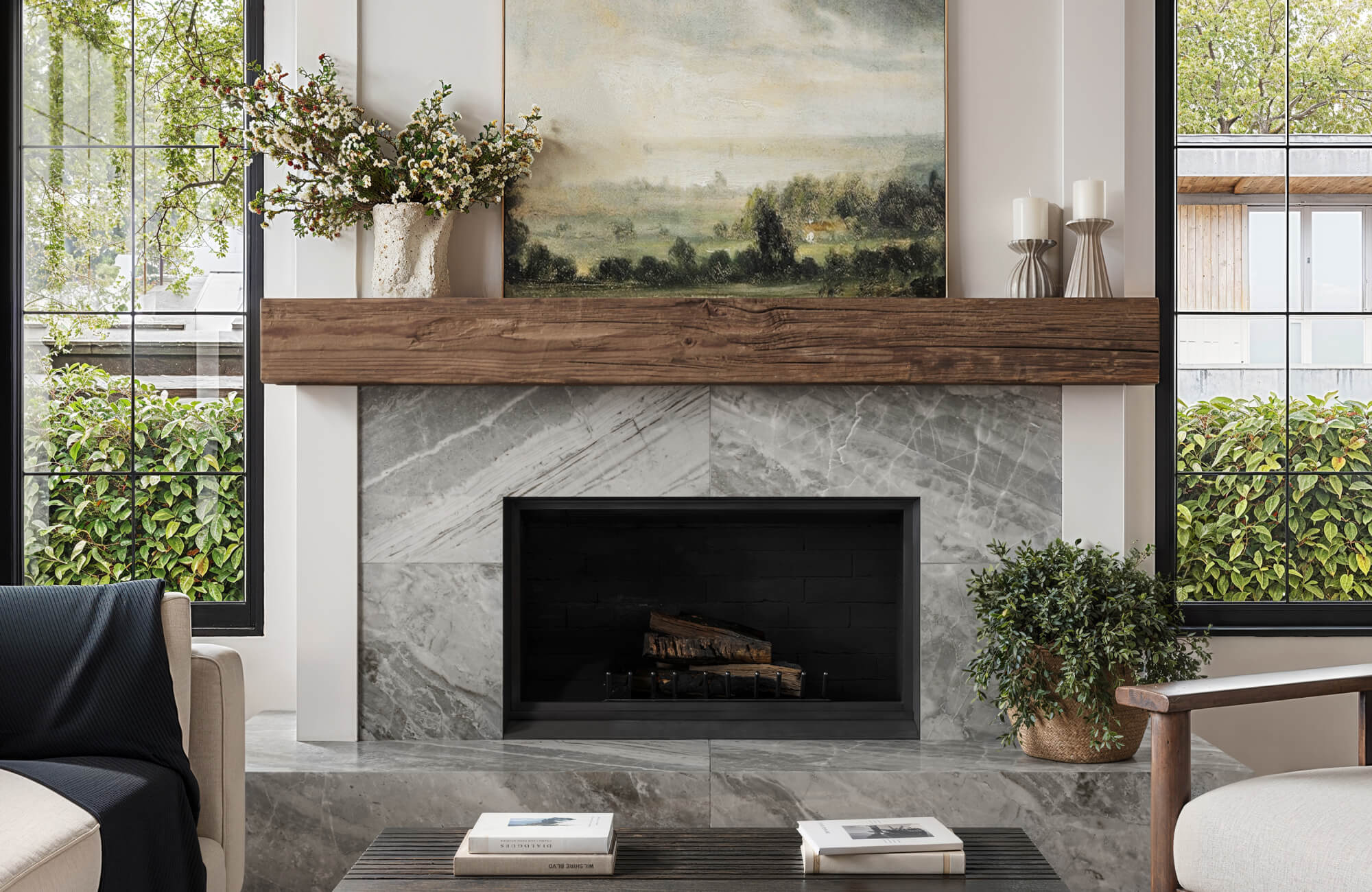 Modern fireplace clad in marble look tile with wood mantel and landscape art in a cozy, contemporary living room.