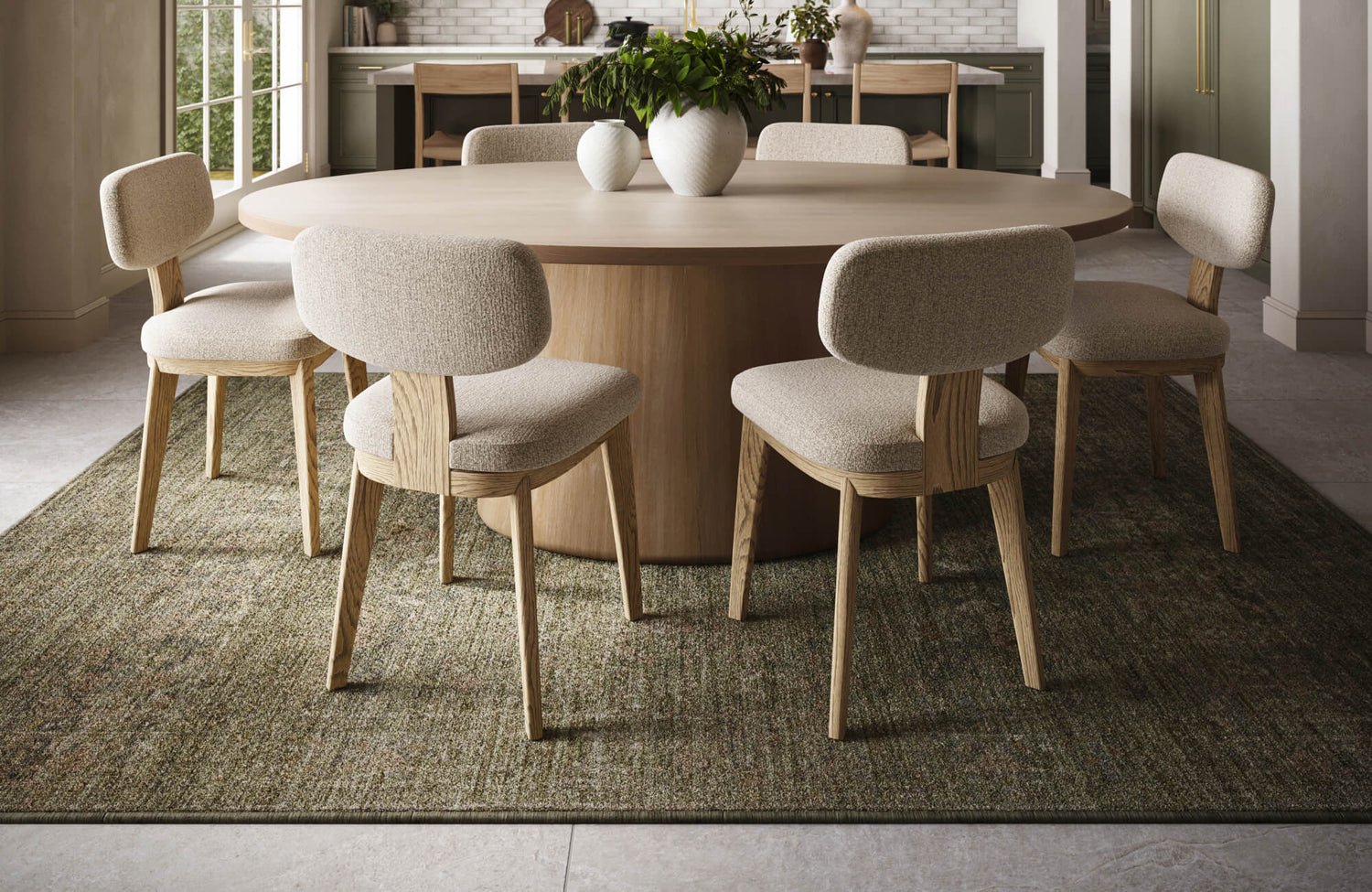 Round wooden dining table with six upholstered chairs on a moss-toned textured rug in a modern kitchen setting.