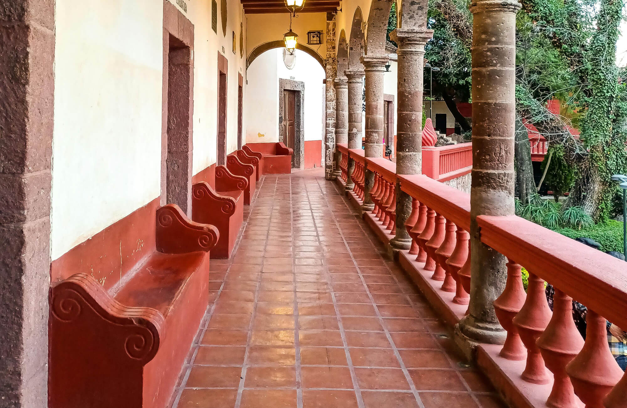 Rustic terracotta tile floor in a colonial-style corridor with arched stone columns and red built-in benches.