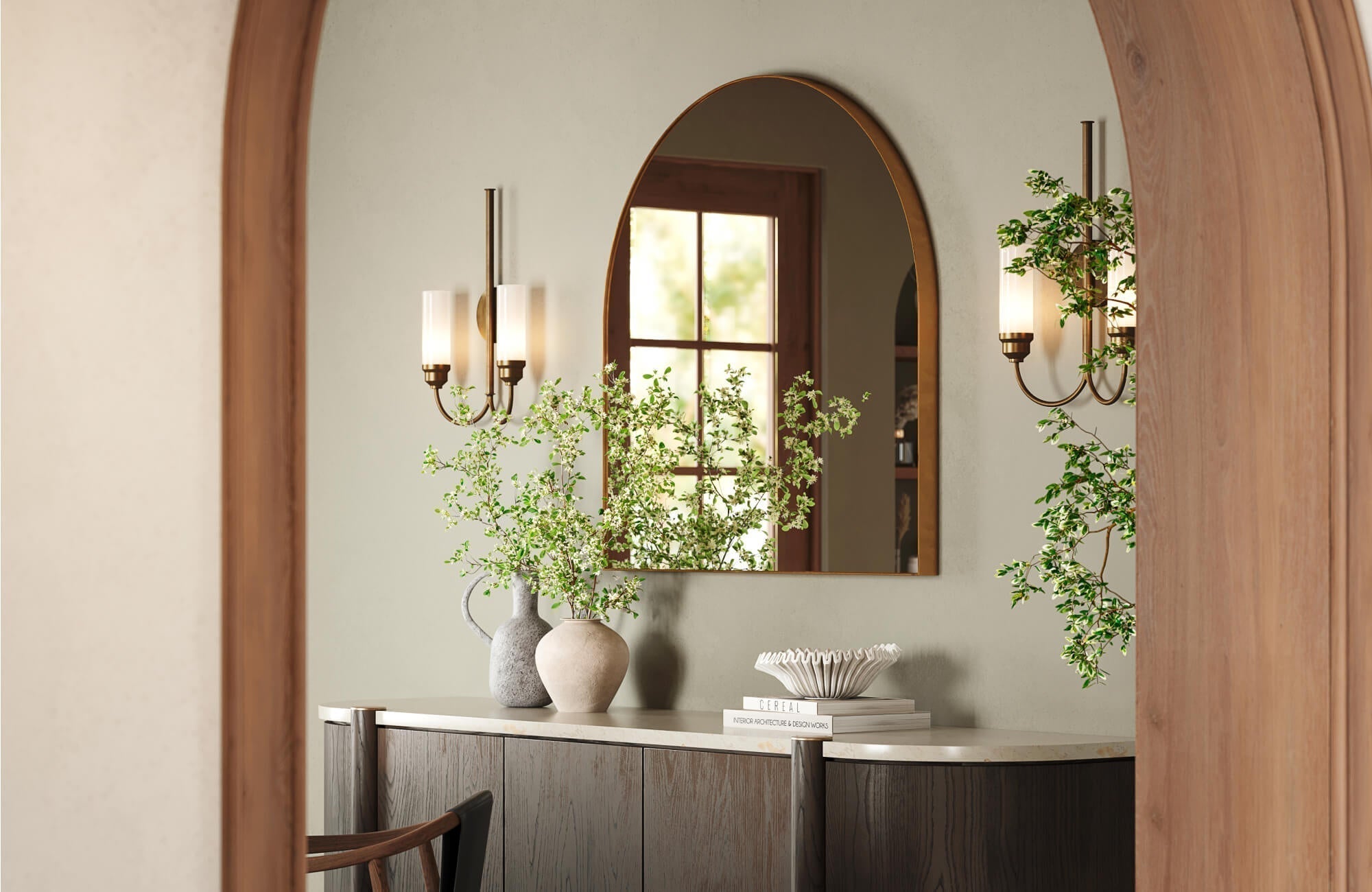 Refined vanity nook with a dark wood cabinet, arched brass mirror, dual glass sconces, and organic accents framed by a warm wood doorway.