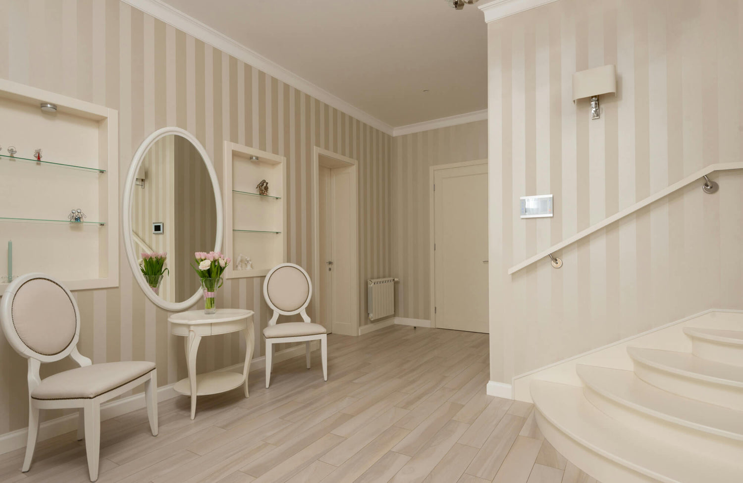 Elegant entryway with light wood-look floor tiles, striped beige walls, and a round mirror above a classic white table.