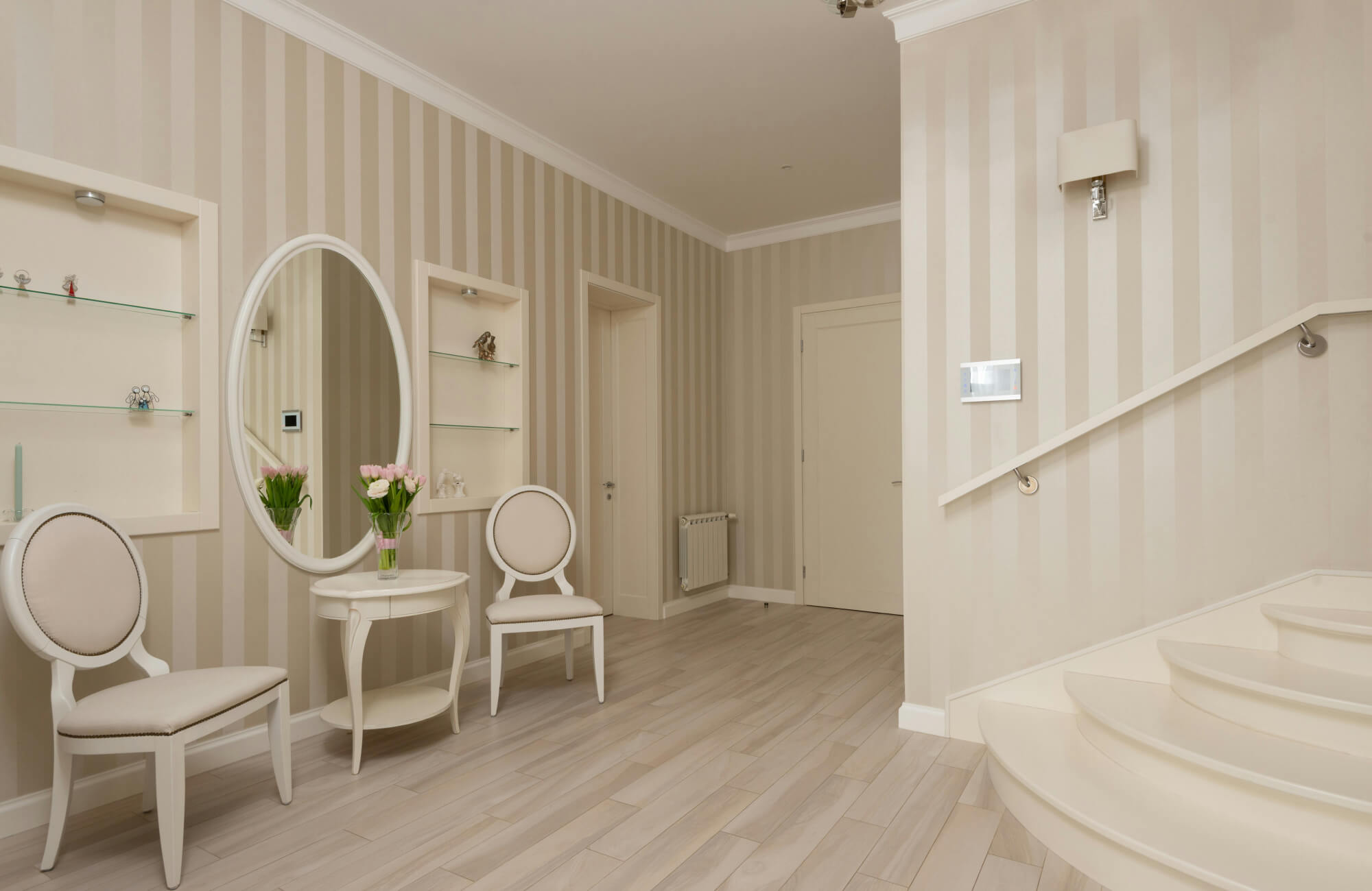 Elegant entryway with light wood-look floor tiles, striped beige walls, and a round mirror above a classic white table.