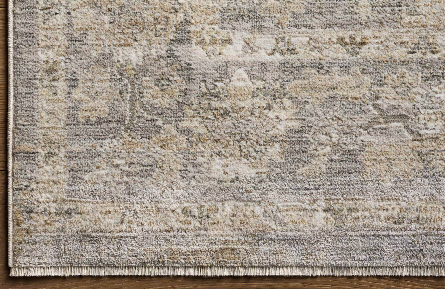 Textured area rug in muted beige, cream, and grey tones with a distressed, vintage-style pattern and subtle fringe edge.