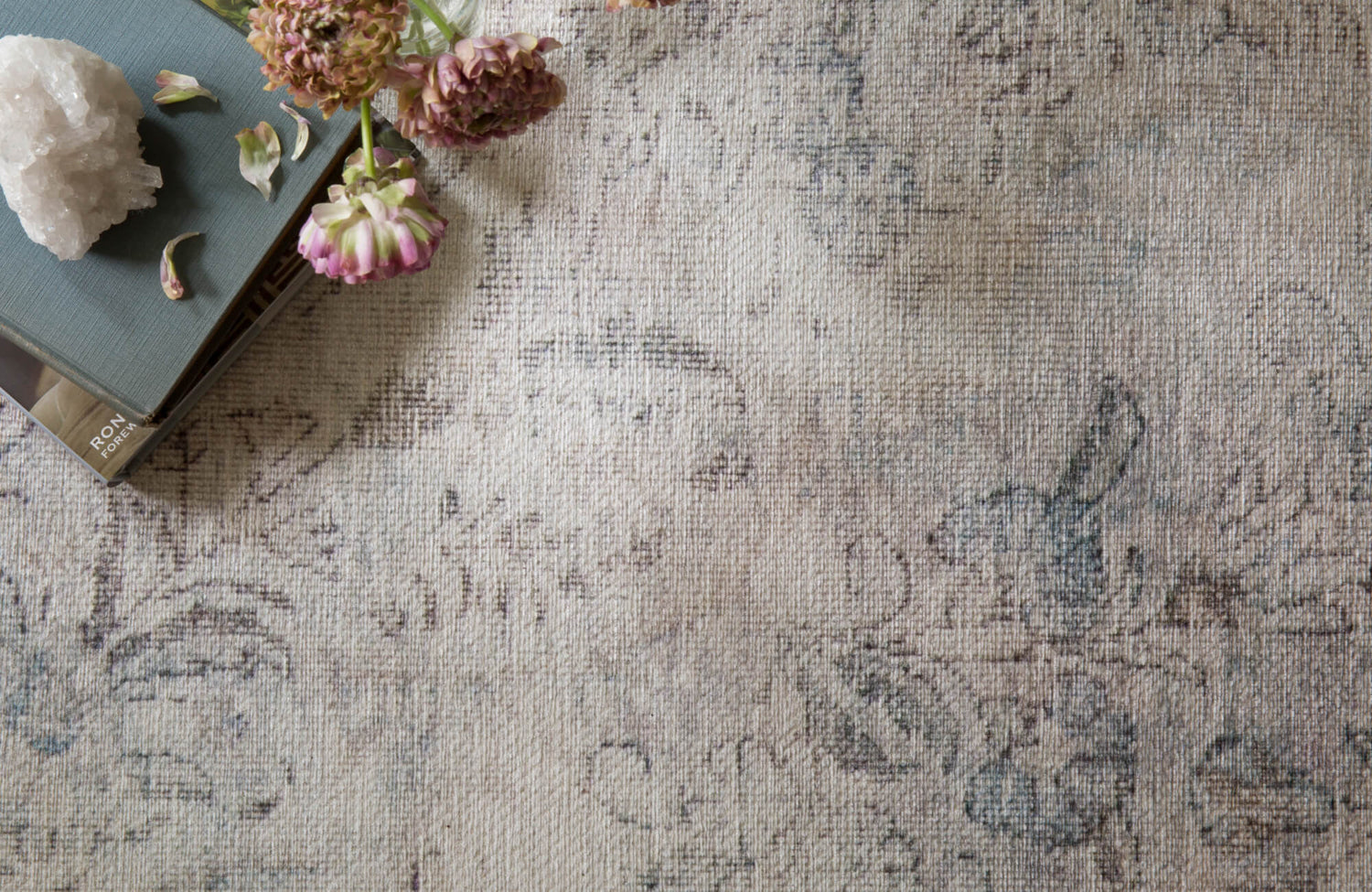 Subtle floral-patterned rug in soft taupe and faded blue tones, evoking a vintage, timeworn elegance.
