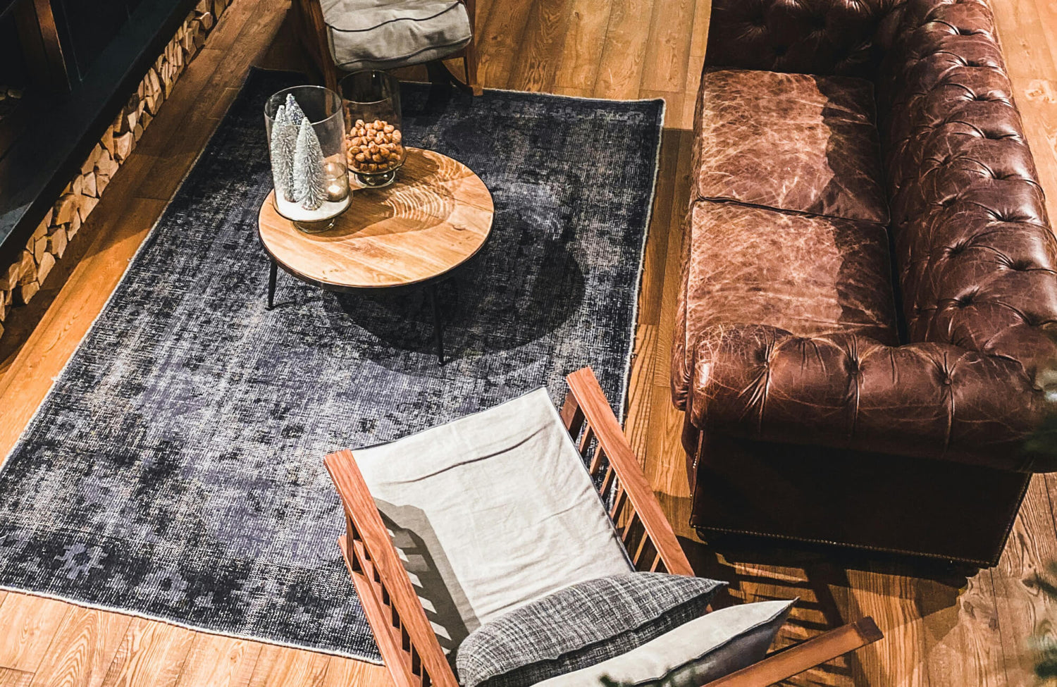 Cozy living room with a vintage brown leather sofa, wood-framed lounge chair, and dark textured rug on warm oak flooring.